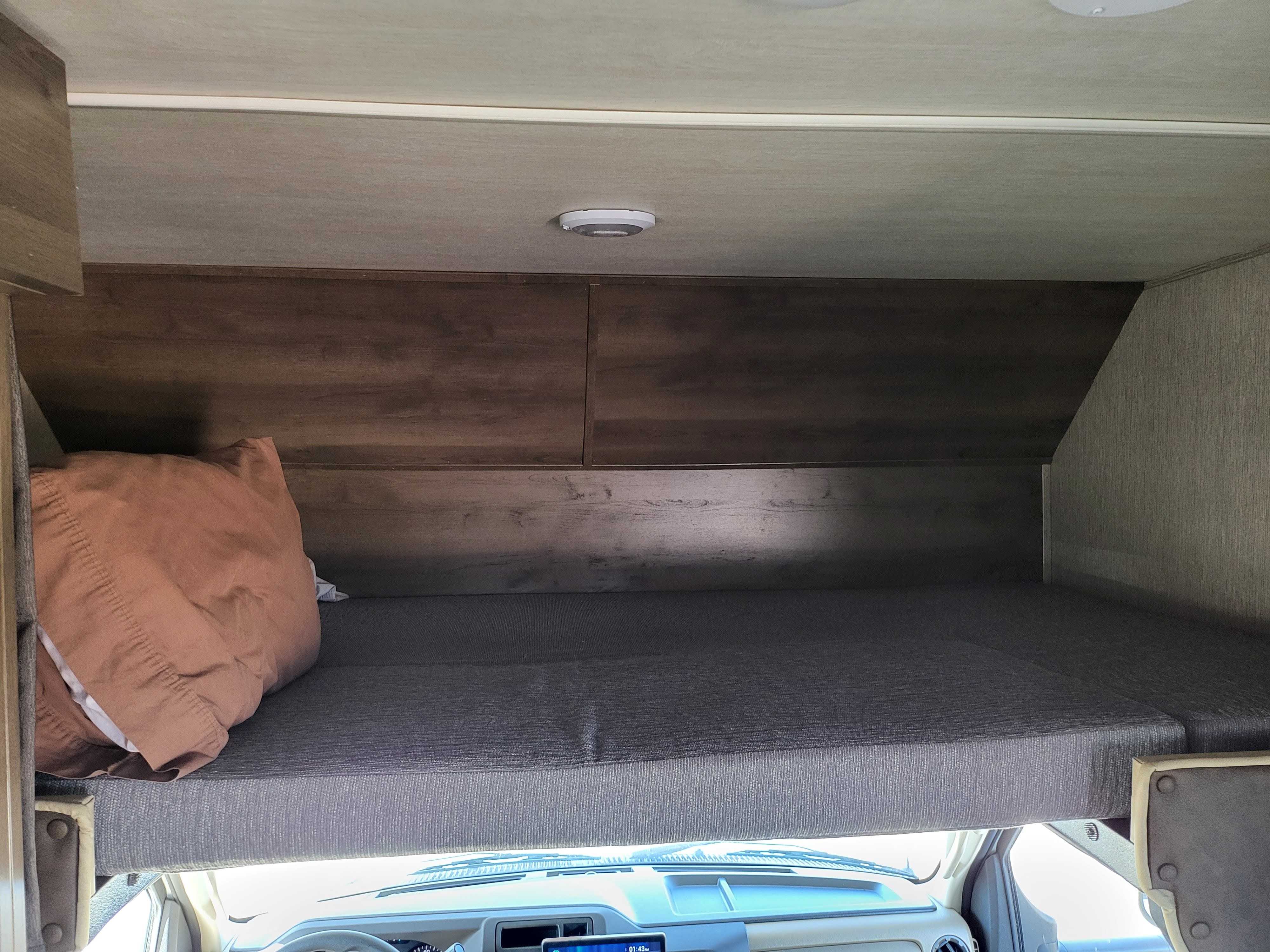 Cozy overhead bunk bed in an RV rental, featuring a mattress and pillow, located above the vehicle's cab.. Nexus RV Phantom 2022