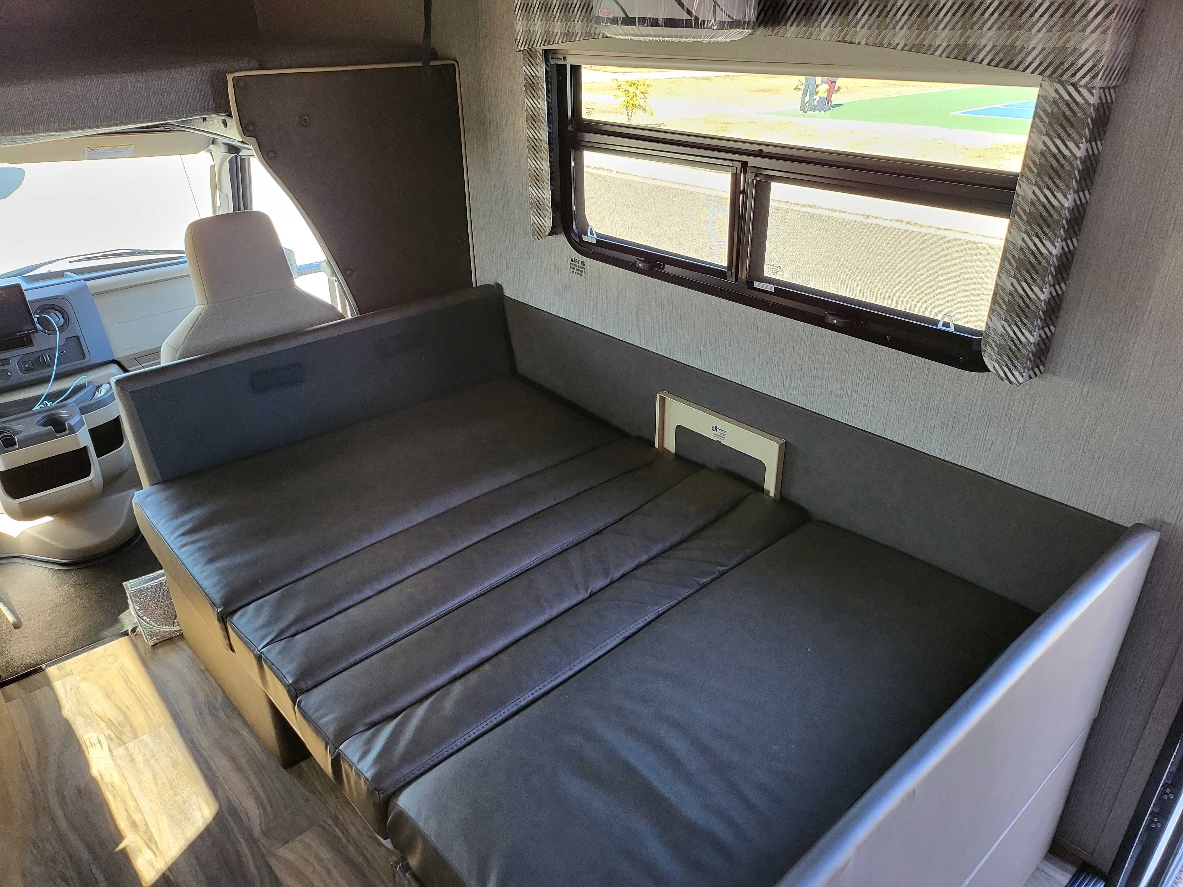 RV rental interior with a versatile fold-out bed, window, and accessible front cab, offering comfort for your journey.. Nexus RV Phantom 2022