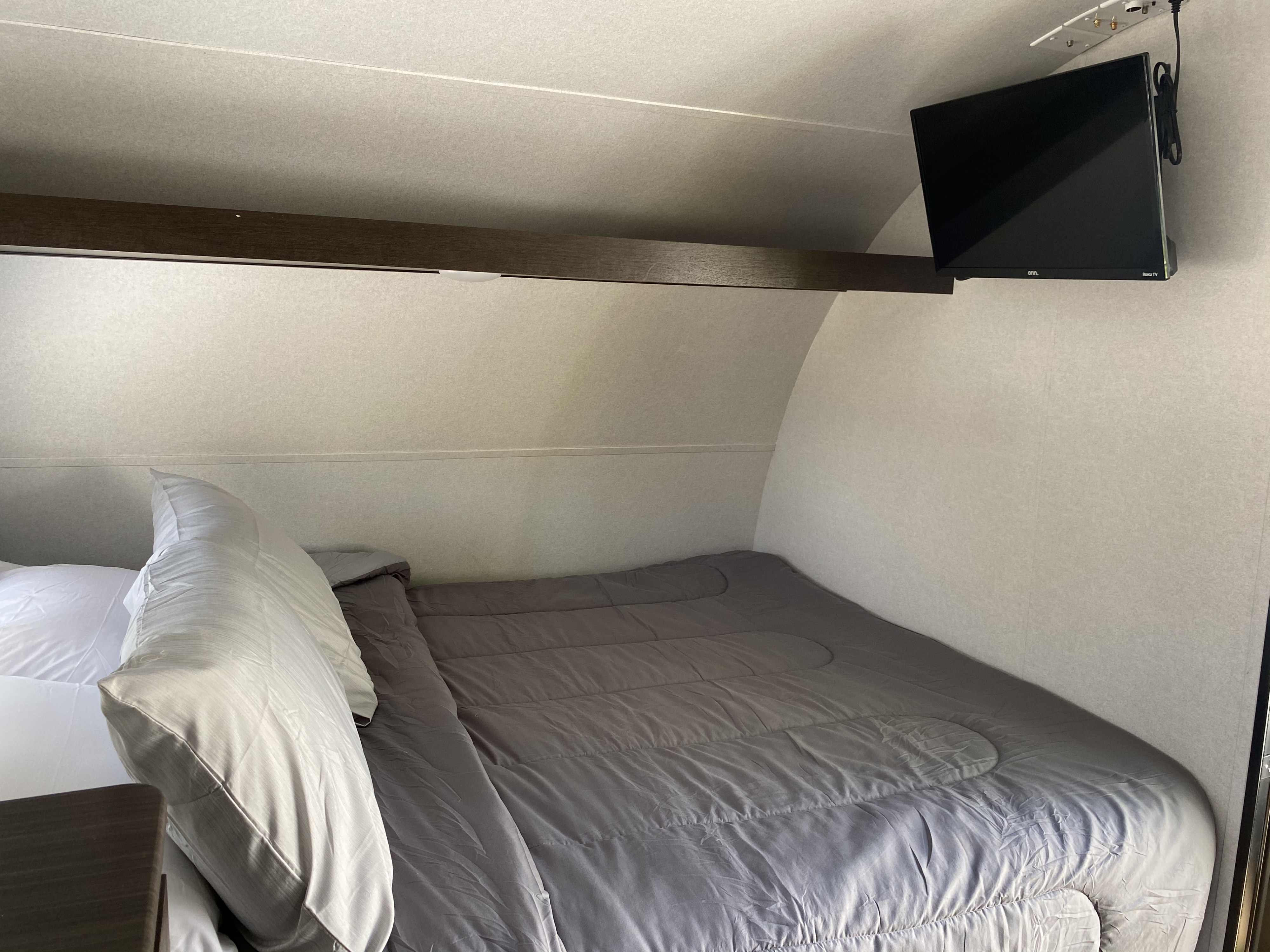 Cozy RV rental sleeping area featuring a made bed with gray comforter and pillows, plus a wall-mounted TV.. Forest River EVO 2020
