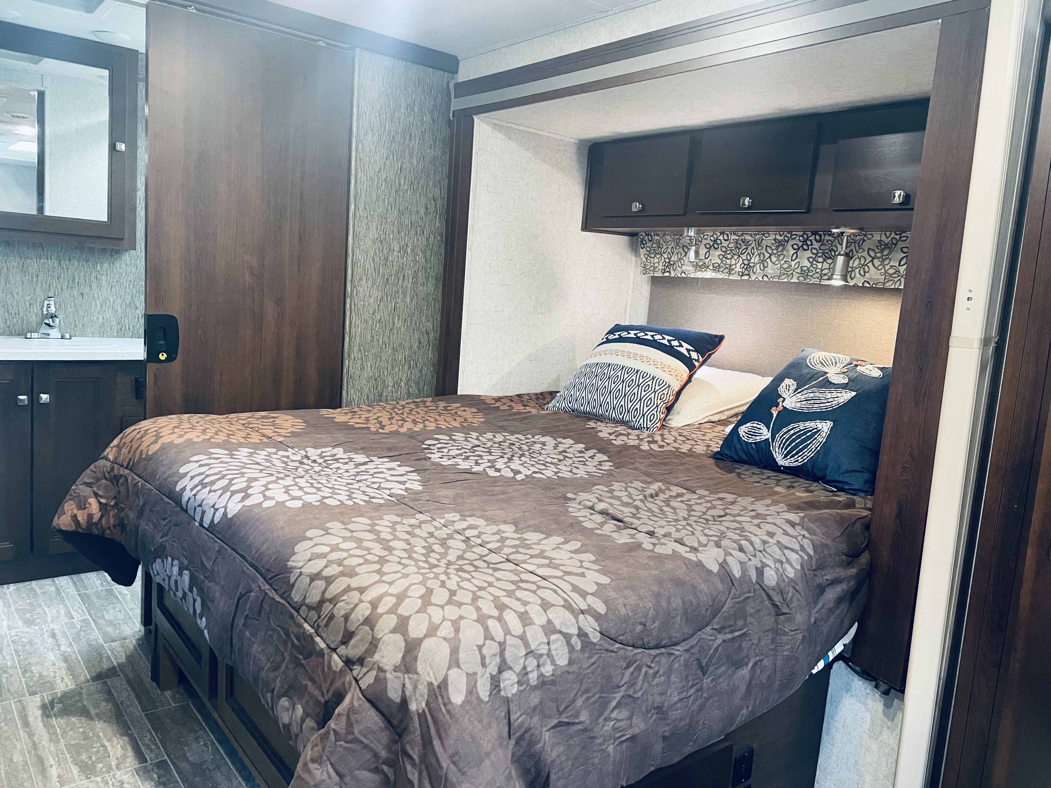 Comfortable RV rental bedroom featuring a patterned bed, overhead storage, and an adjacent sink with mirror.. Forest River Forester 2018