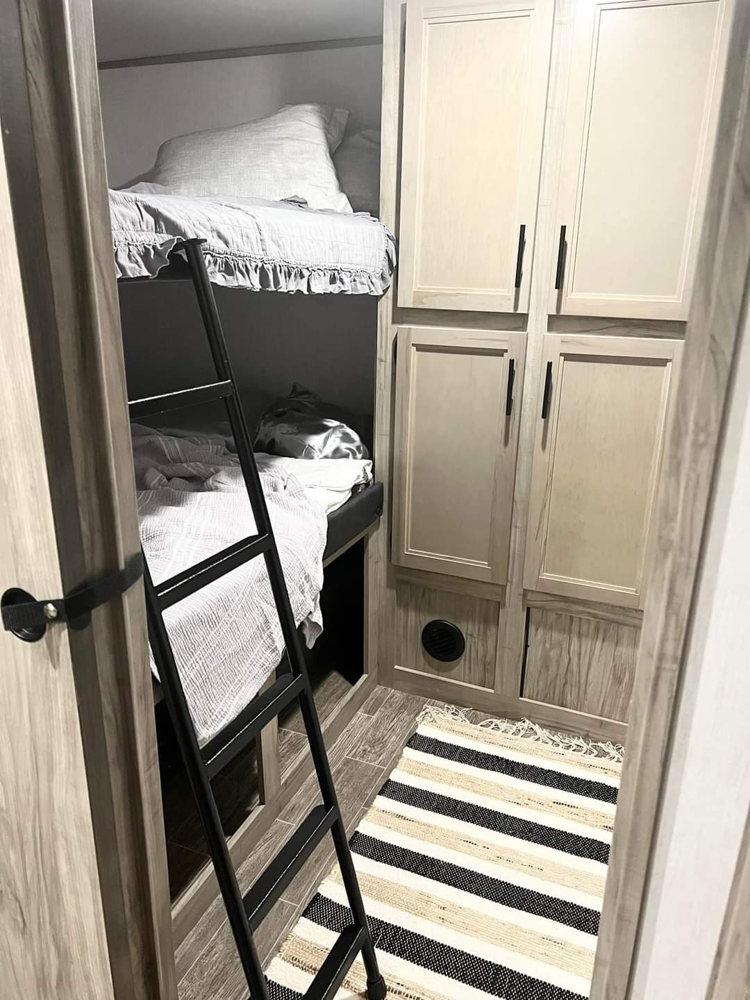 Cozy bunk beds and storage in an RV rental, featuring a ladder and a striped rug on the floor.. Forest River Cherokee Alpha Wolf 2021
