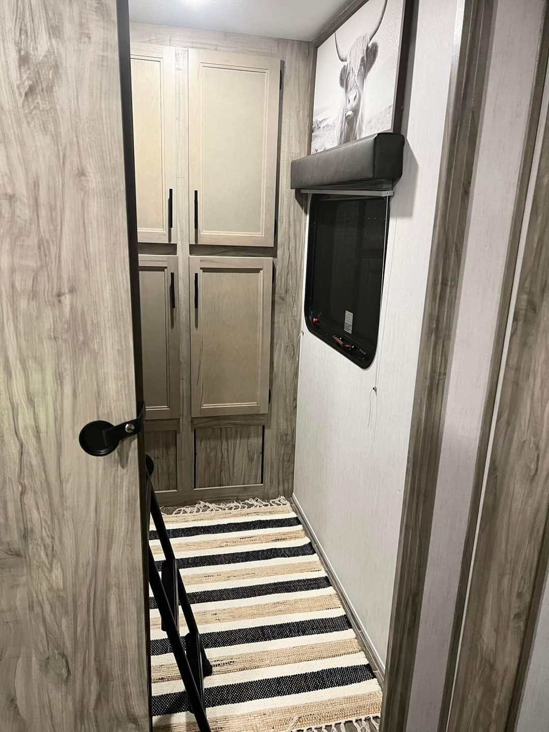 Experience comfort in this RV rental hallway featuring light wood cabinetry, a window with art, and a stylish striped rug.. Forest River Cherokee Alpha Wolf 2021