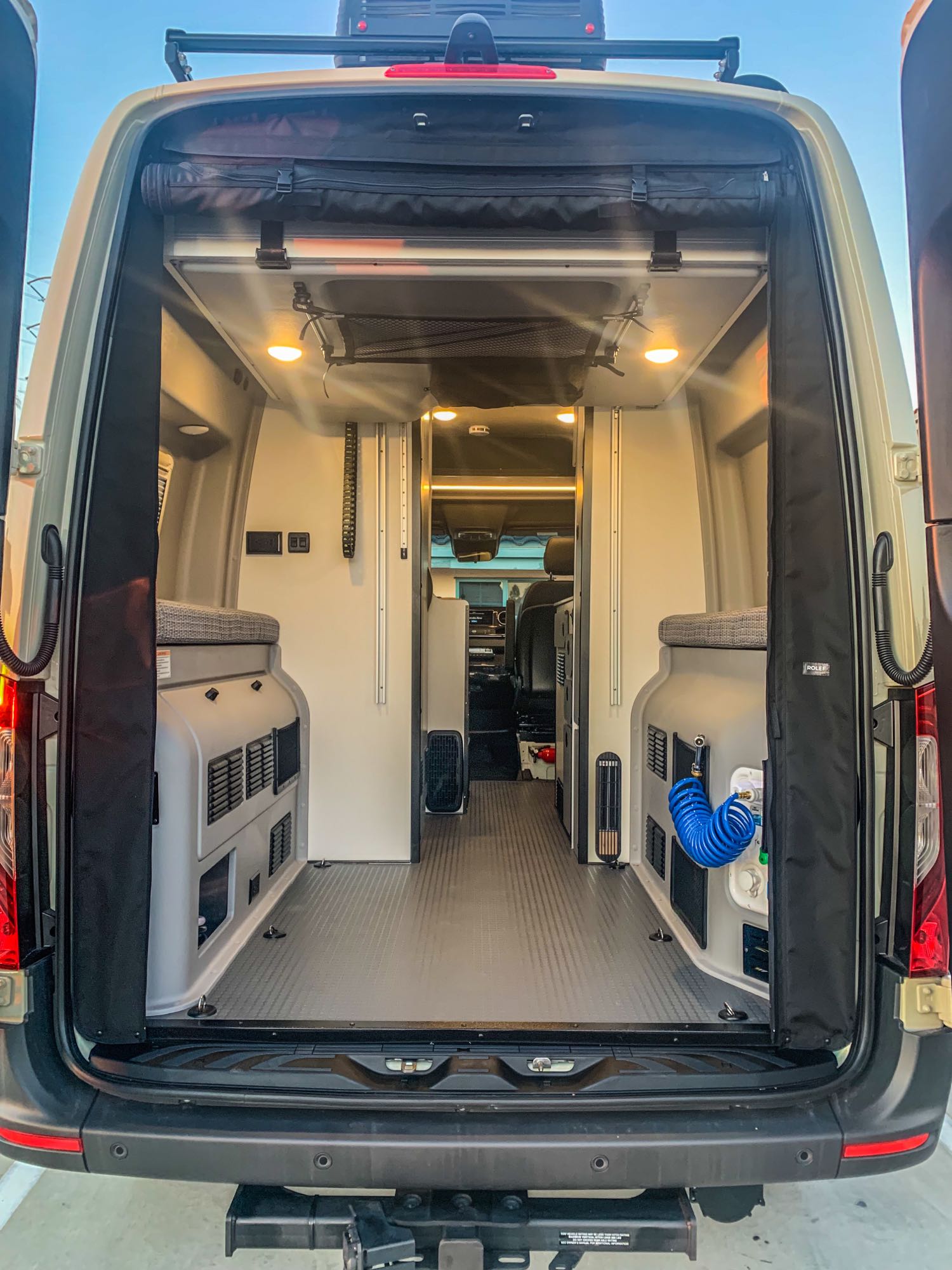 RV rental camper van: Rear view shows a well-equipped, light-toned interior with configurable benches, overhead storage, and utility hookups.. Winnebago Revel 2022