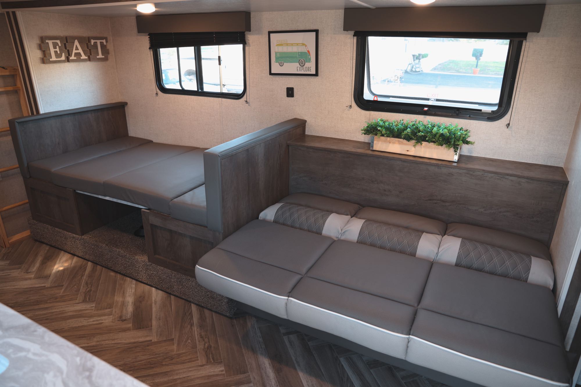 Modern RV rental interior with convertible dinette seating, a bunk bed, and warm wood tones.. Forest River Wildwood X-Lite 2021