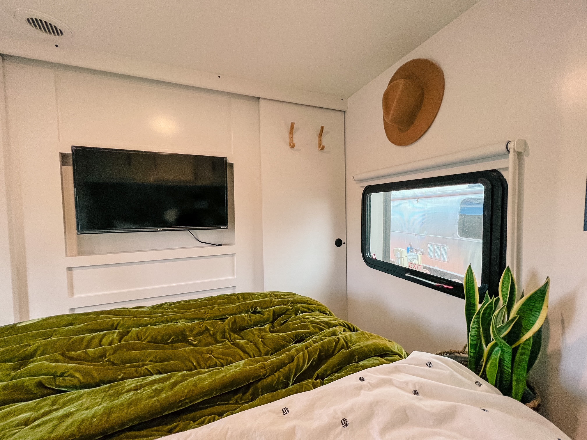 Cozy RV rental bedroom featuring a green velvet bed, mounted TV, and plant. Modern interior for comfortable travel.. Keystone RV Passport Grand Touring 2017