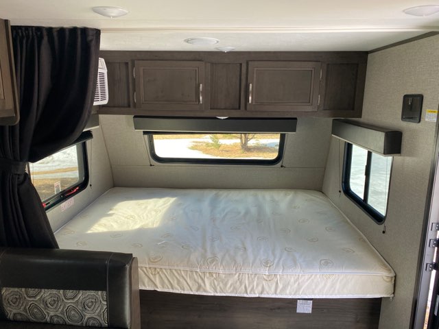 Interior of an RV rental showing a compact bedroom area with a bed, overhead cabinets, and side windows.. Jayco Jay Flight 2020