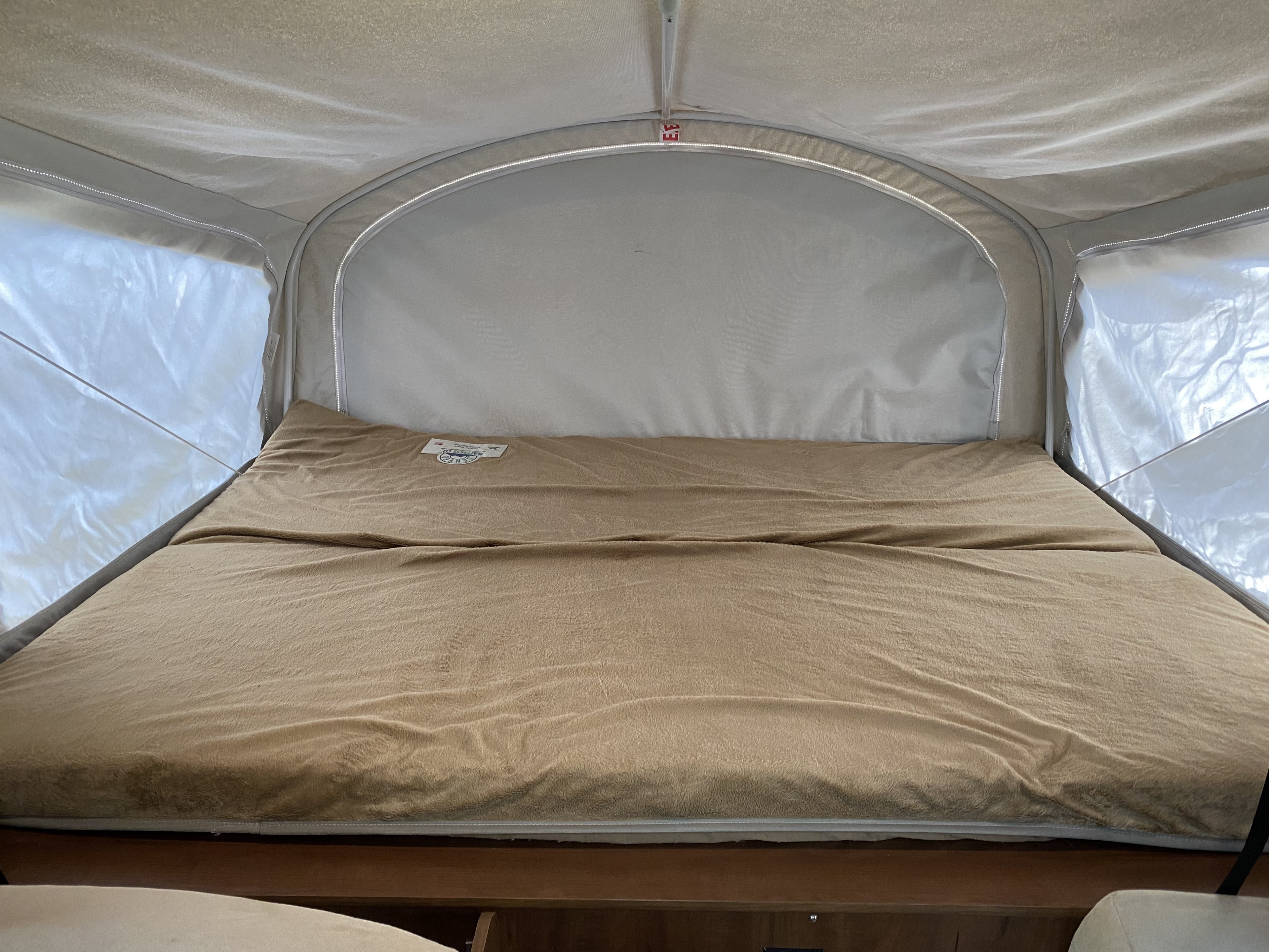 Cozy bed inside an RV rental pop-up camper, perfect for camping. Features soft bedding & interior tent lighting.. Jayco Jay Feather 2016
