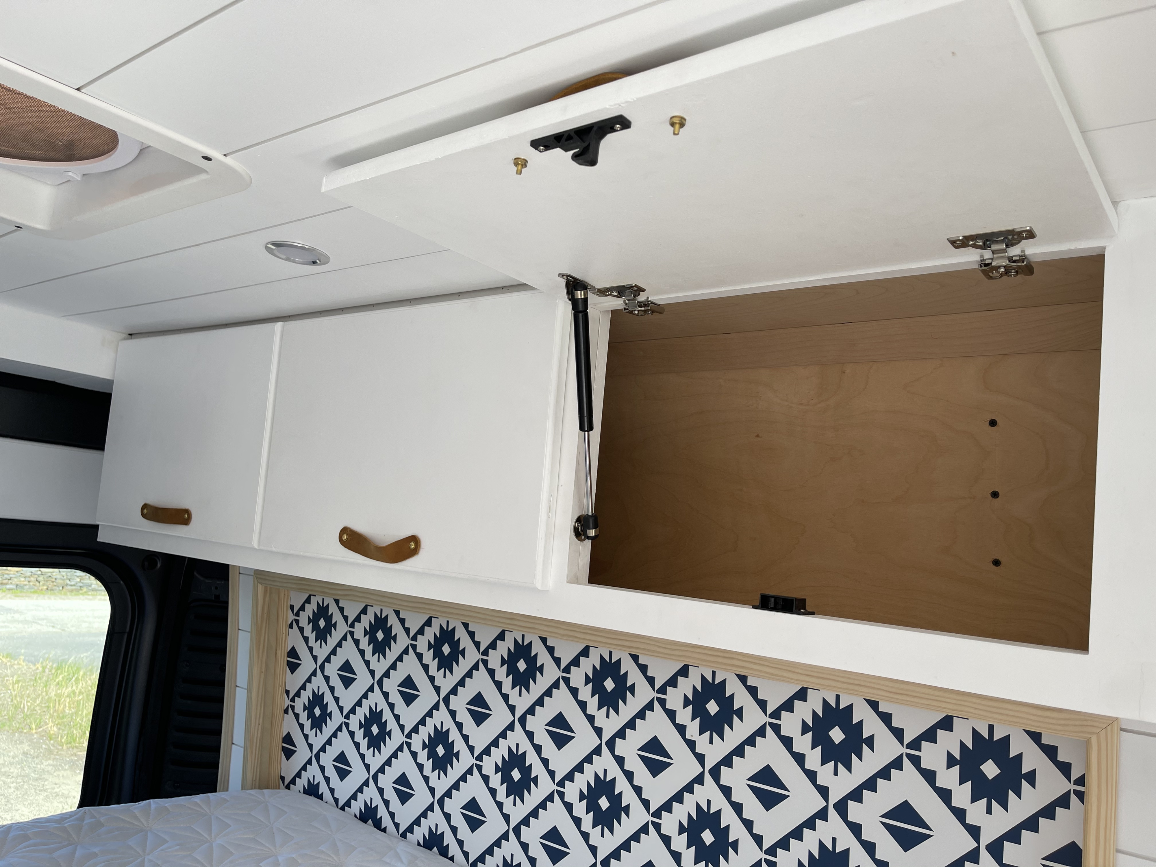 RV rental interior: white overhead cabinets, one open with gas strut, patterned headboard, and cozy bed.. Dodge Ram PROMASTER 2015