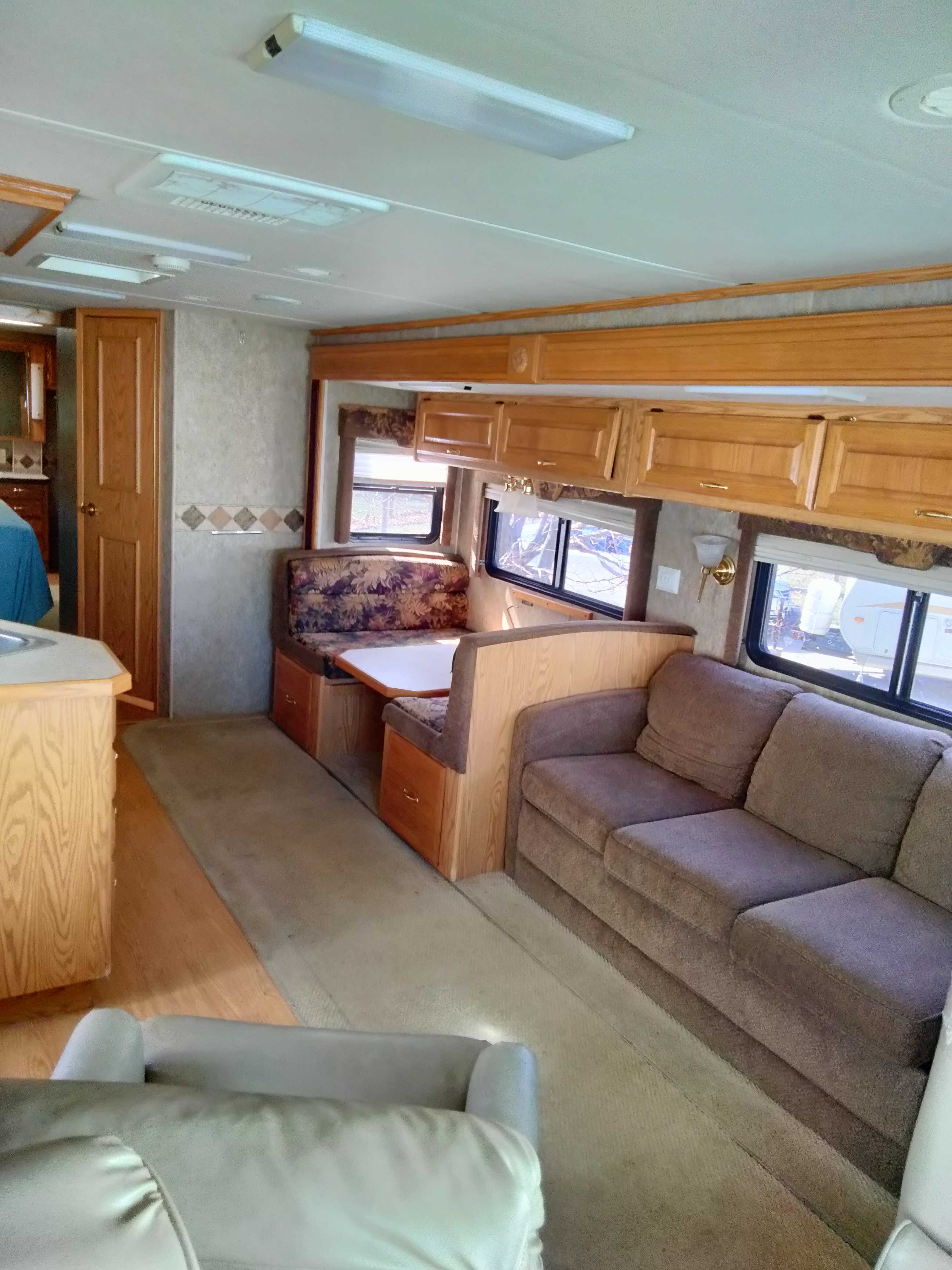 Spacious RV rental interior featuring a cozy living area with a sofa, a dining booth, and wooden cabinetry.. Holiday Rambler Admiral SE 2005