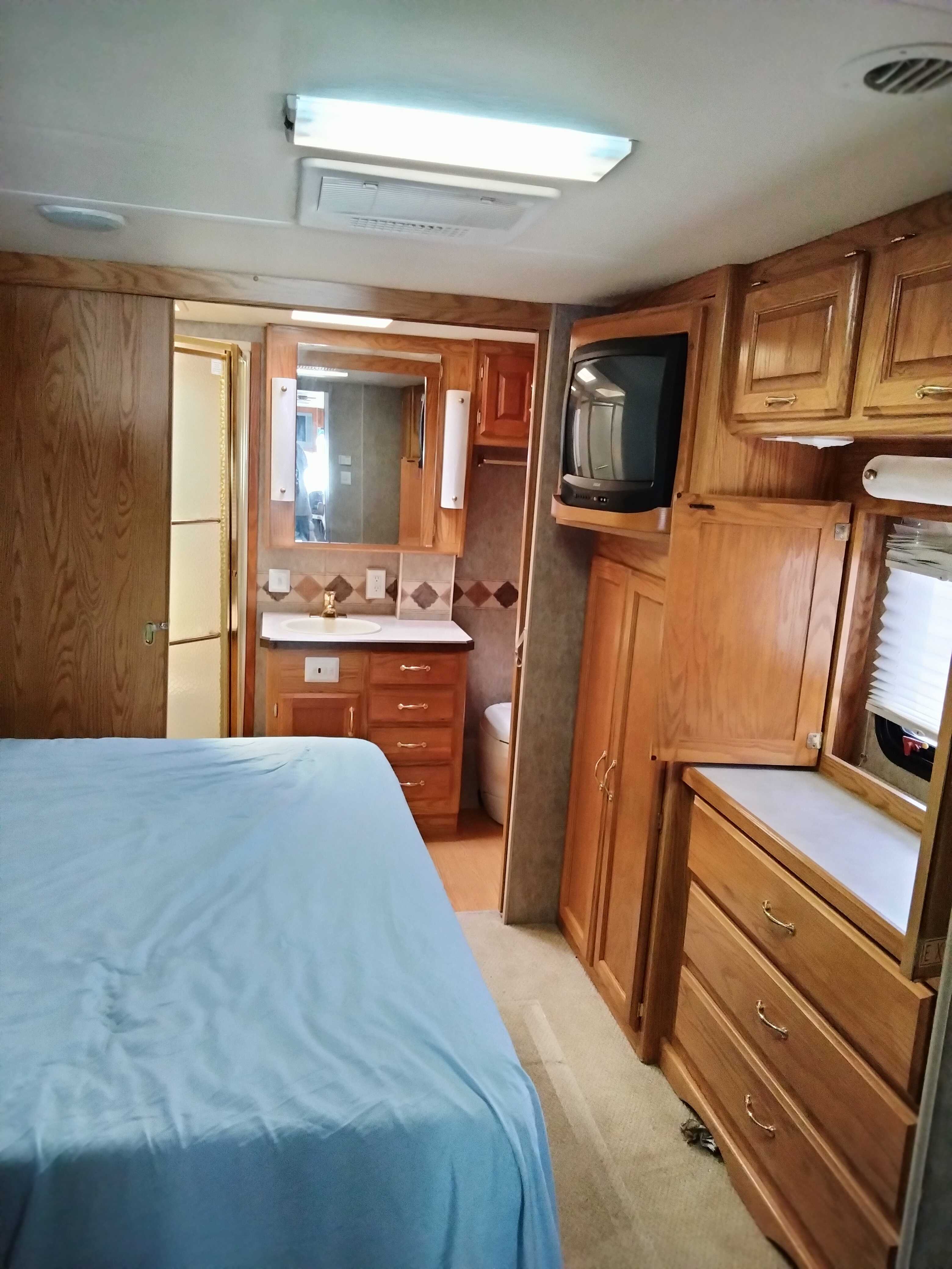 RV rental bedroom featuring a bed, integrated bathroom with vanity/shower, TV, & wooden storage cabinets.. Holiday Rambler Admiral SE 2005