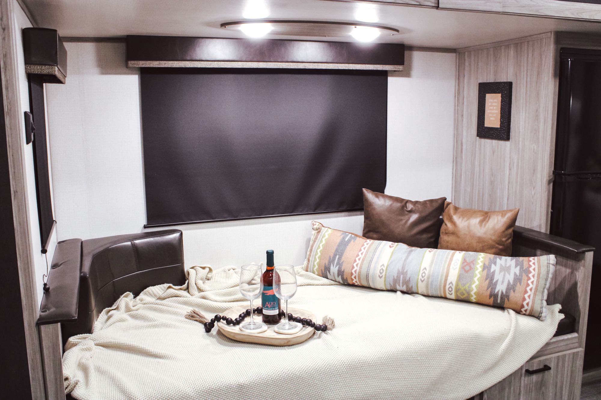 Relax in this cozy RV rental with a comfortable bed, decorative pillows, and a wine setup on a tray.. Keystone RV Passport GT 2021