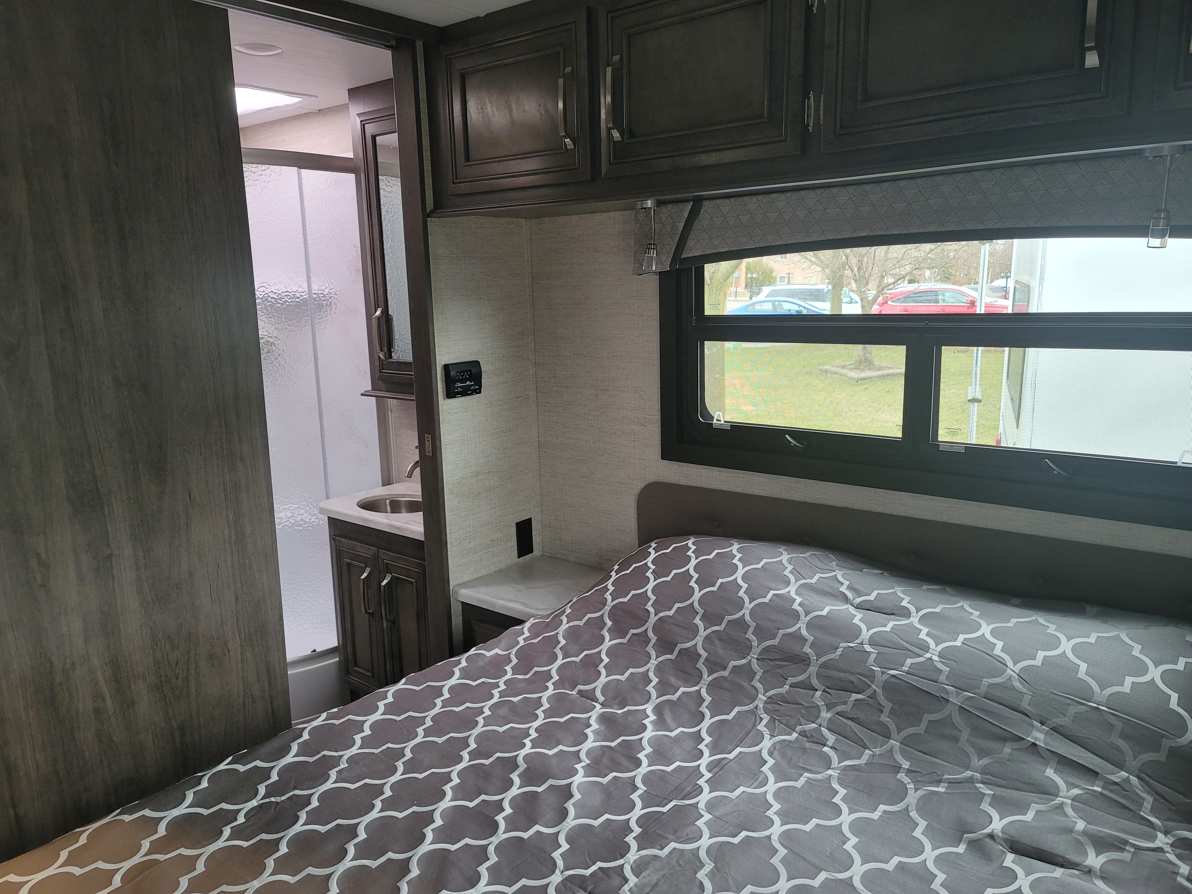 Spacious RV rental interior featuring a cozy bedroom with patterned bedding, overhead cabinets, and an adjoining bathroom.. Jayco Prestige 31FP 2022