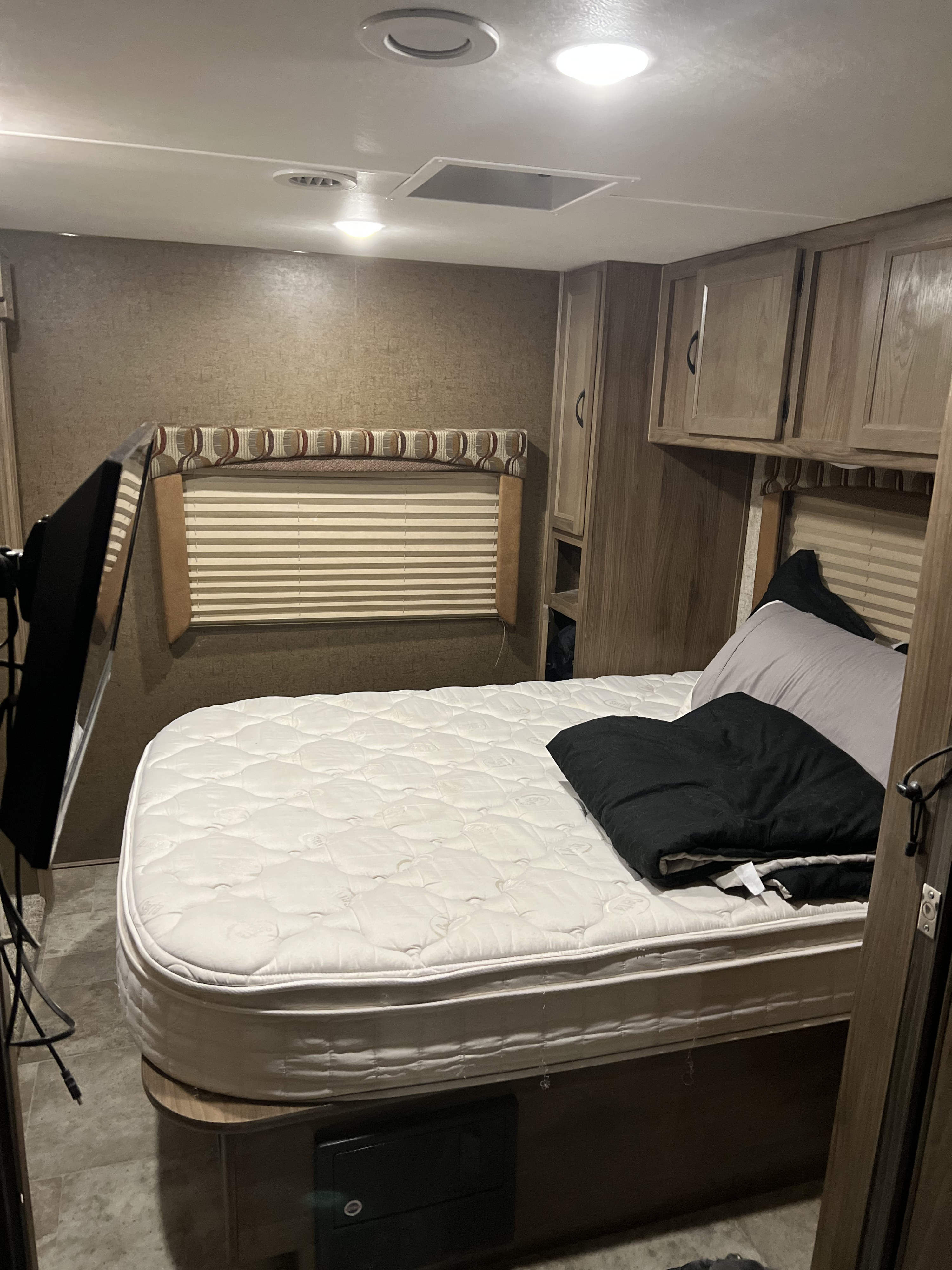 RV rental bedroom setup with a large quilted mattress, overhead storage, and window with blinds.. Other Other 2018