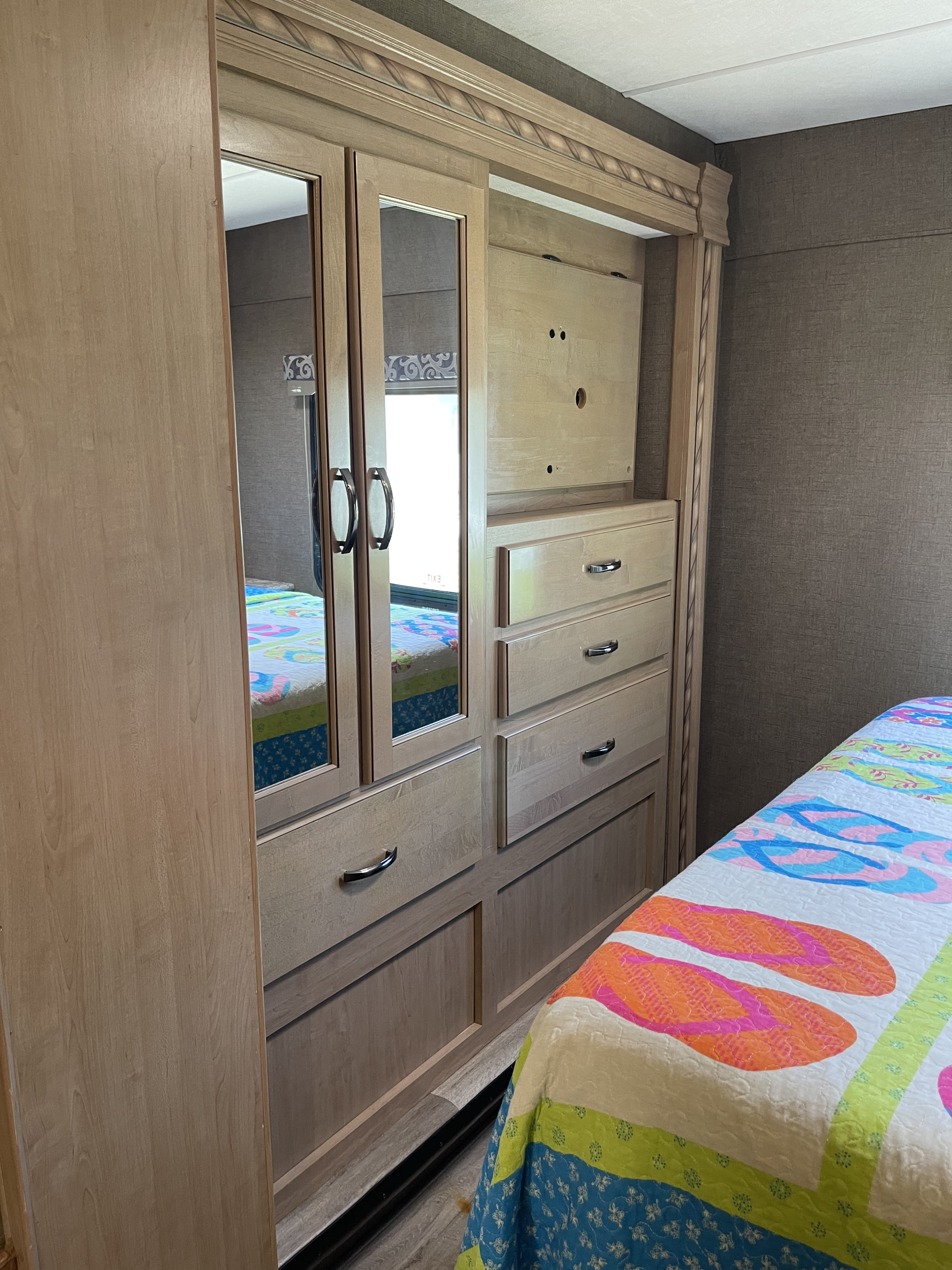 Inside an RV rental bedroom: light wood wardrobe with mirrored doors, drawers, and a vibrant quilt on the bed.. Thor Four Winds 2018