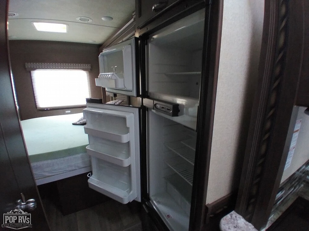 Inside this **RV rental**: a compact, open refrigerator/freezer & a bed, showing the living space amenities.. Thor Motor Coach Freedom Elite 2018