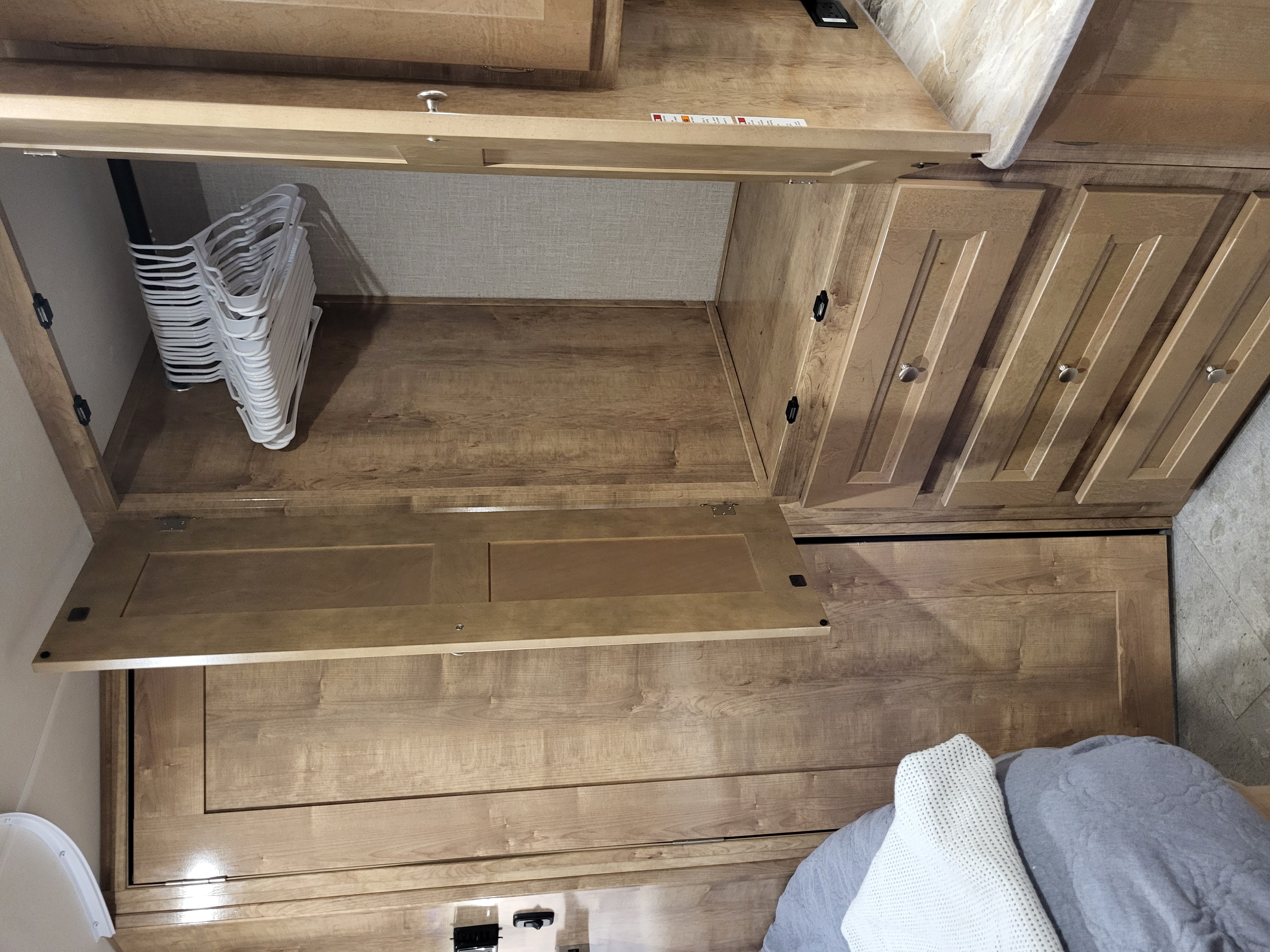 RV rental's spacious bedroom closet with empty hangers, wood cabinetry, and a cozy bed area for travelers.. Coachmen Leprechaun 230CB 2020