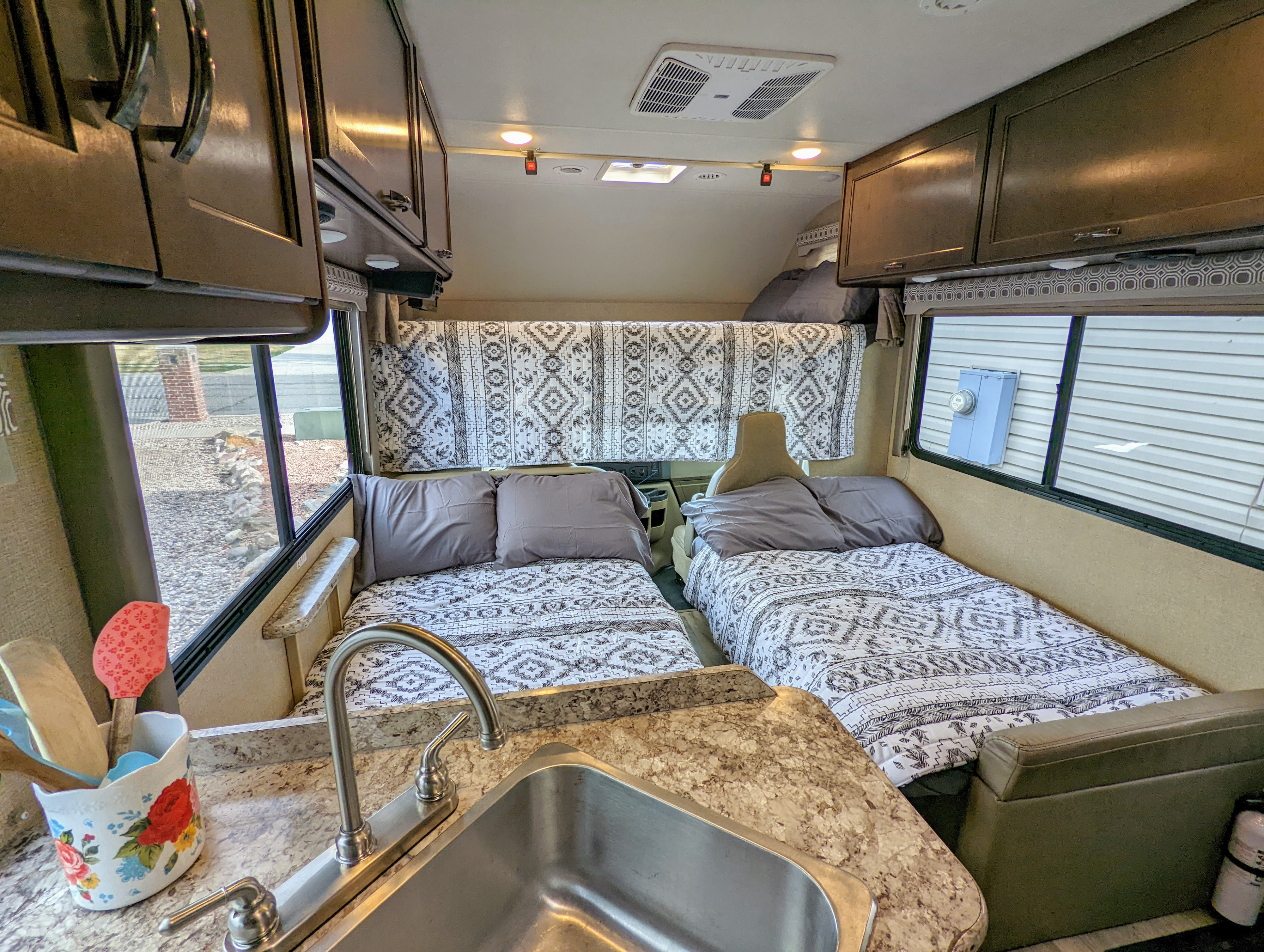 Inside a comfortable **RV rental**, showing two patterned beds, an equipped kitchen with a sink, and overhead cabinets for storage.. Thor Four Winds 2020