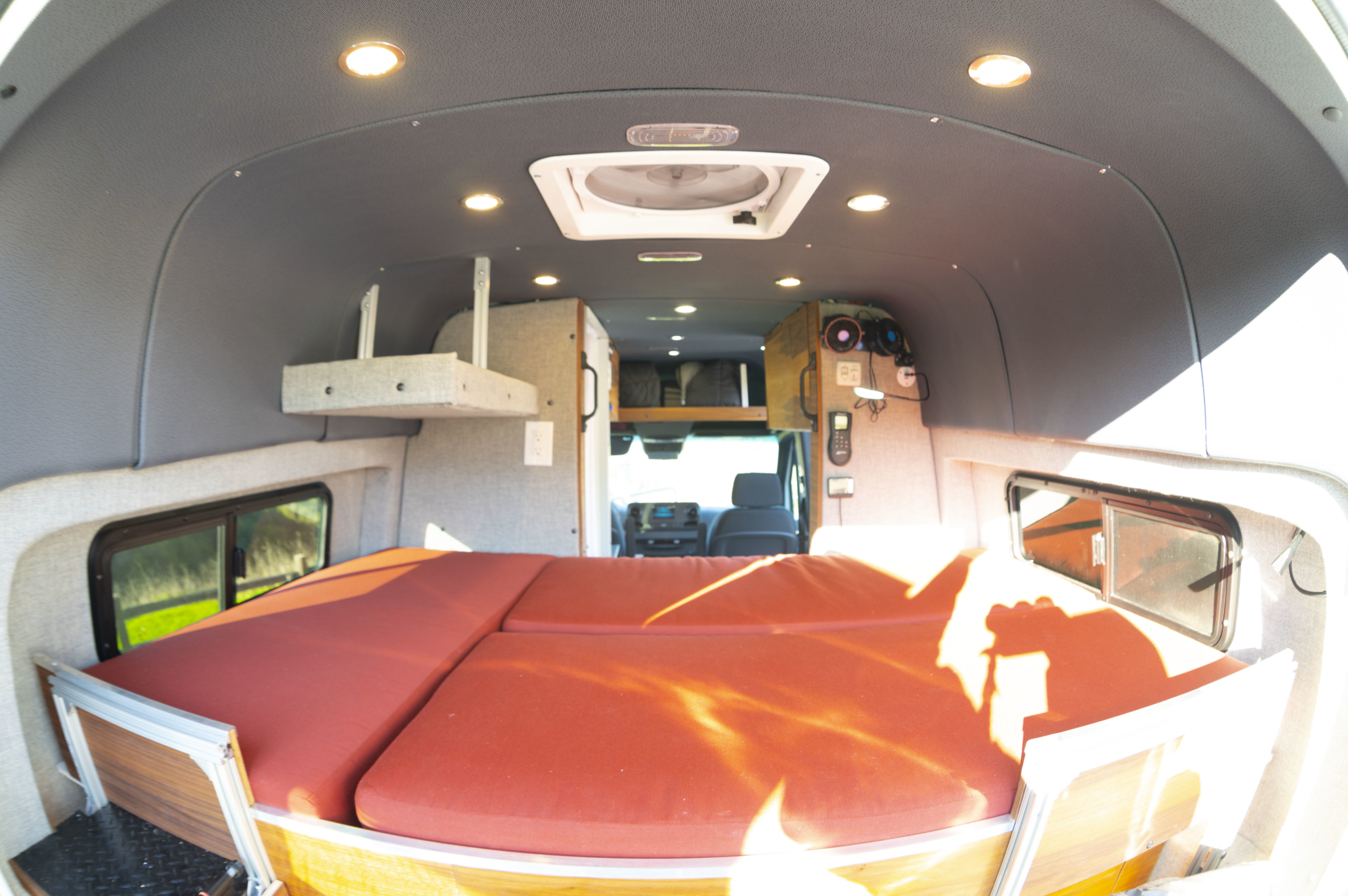 Inside an RV rental camper van, featuring a bright interior, comfortable red bed, overhead lights, and storage shelves.. Mercedes-Benz Sprinter 2019