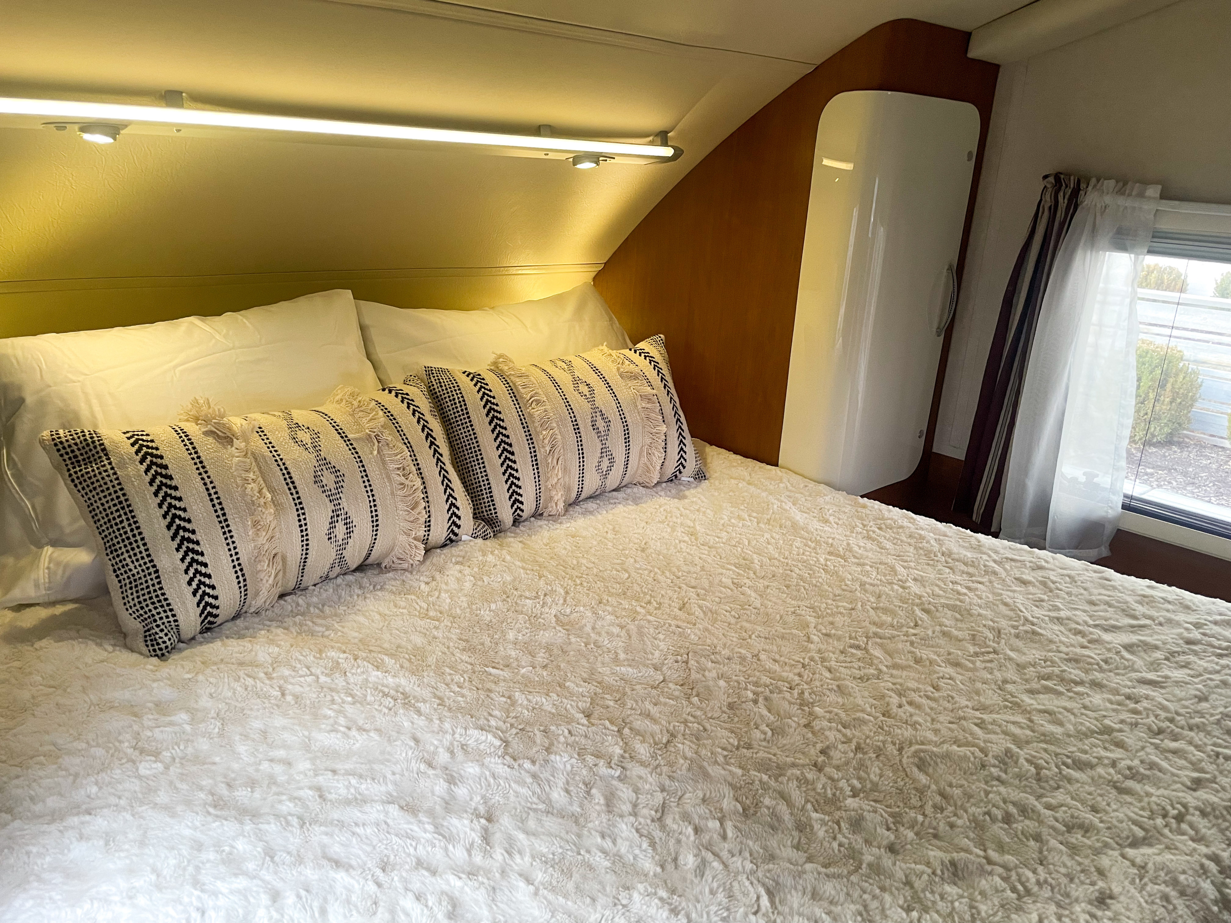 Cozy RV rental bedroom featuring a comfortable bed with a fluffy comforter, patterned pillows, and ambient lighting.. Evergreen Element 2013