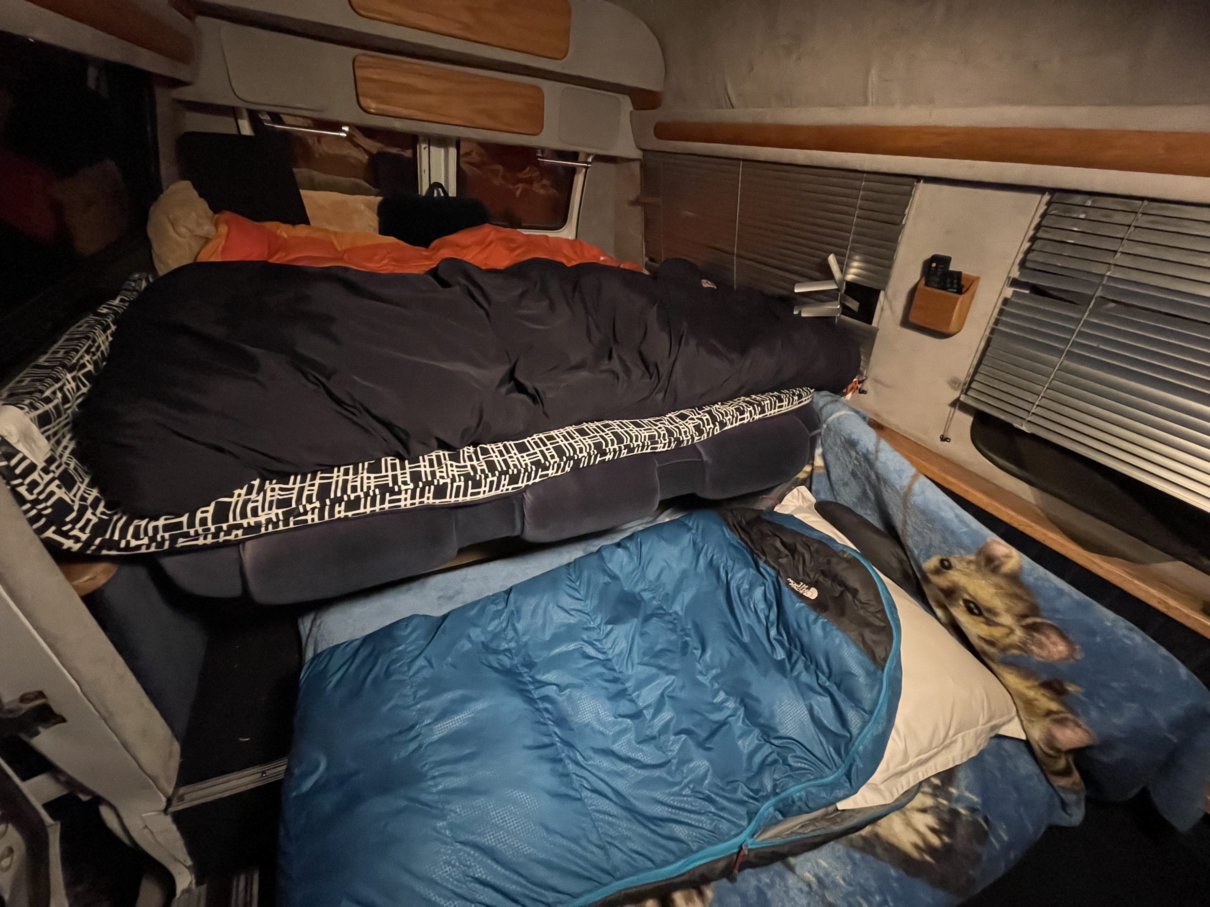 Inside this RV rental, two beds are stacked: a top black sleeping bag, and a blue one below with a giraffe blanket.. Ford Econoline 1990