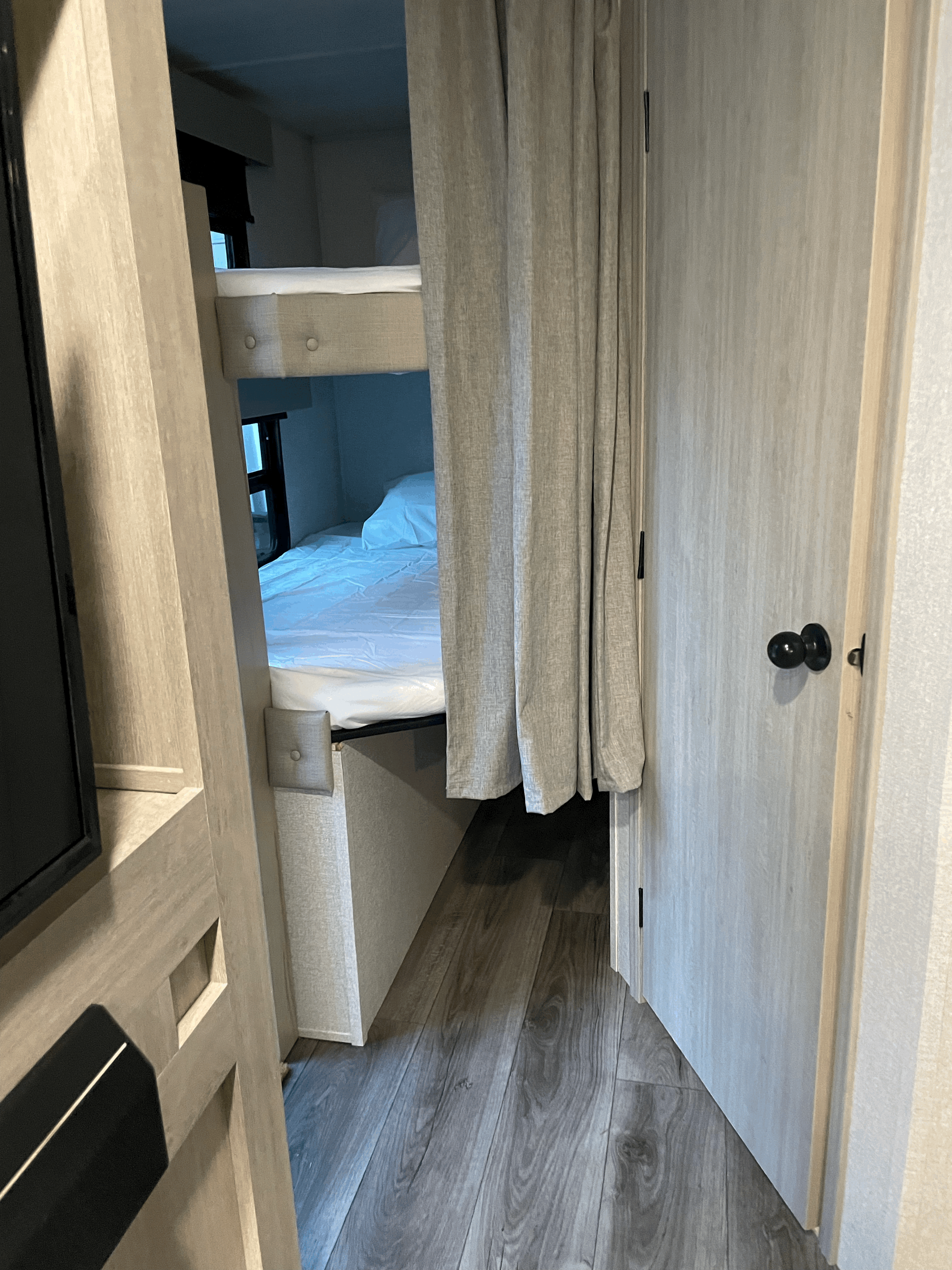 RV rental: Two compact bunk beds with white bedding, light gray privacy curtain, and wood-look flooring visible.. East to West Alta 2022