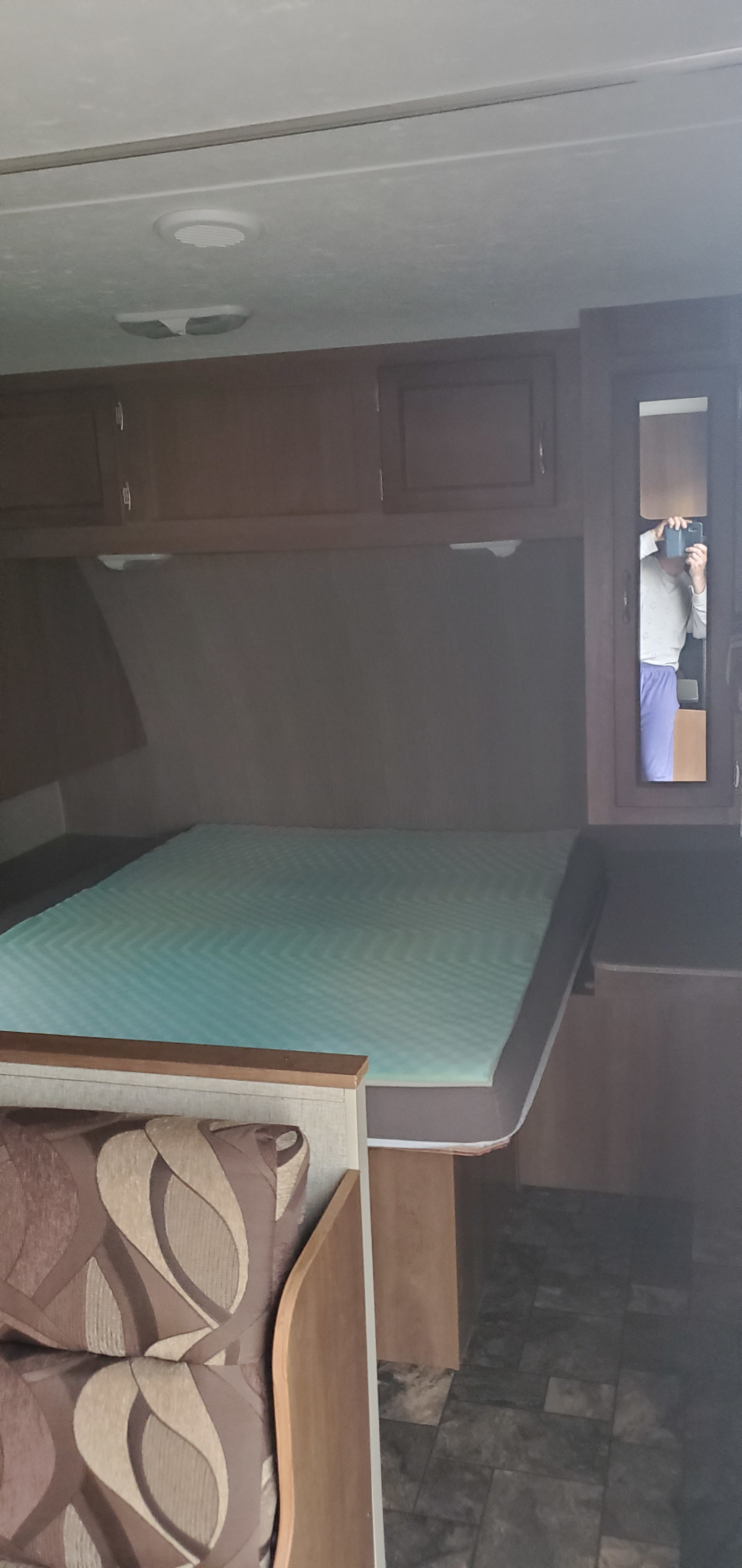 RV rental interior featuring a bed with a light blue topper, wooden cabinets, and a patterned seating area.. Coachmen Catalina 2015
