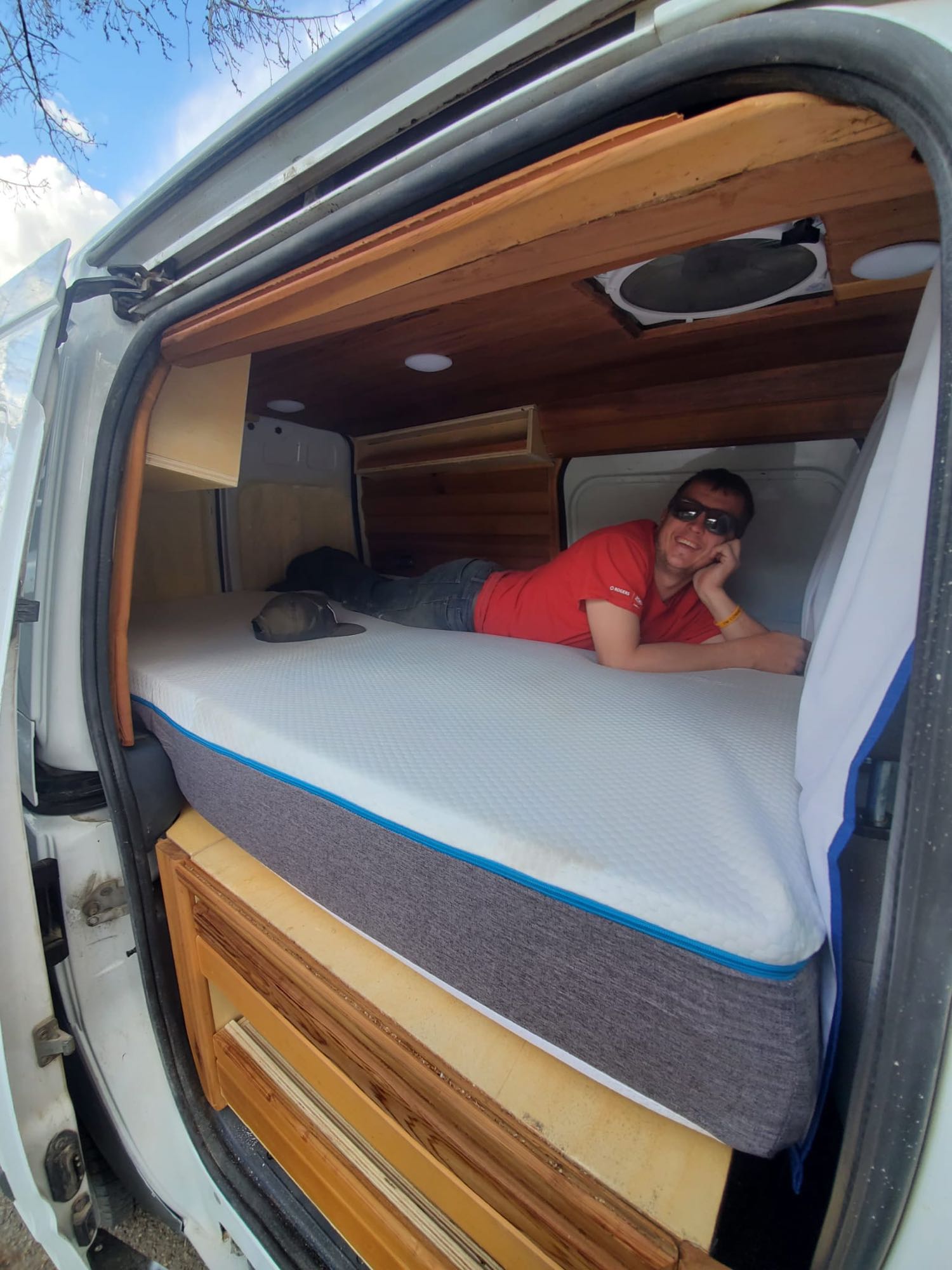 Man relaxes on a comfy mattress in a wood-paneled custom RV rental. Experience cozy camper van living!. Ford Transit 2010