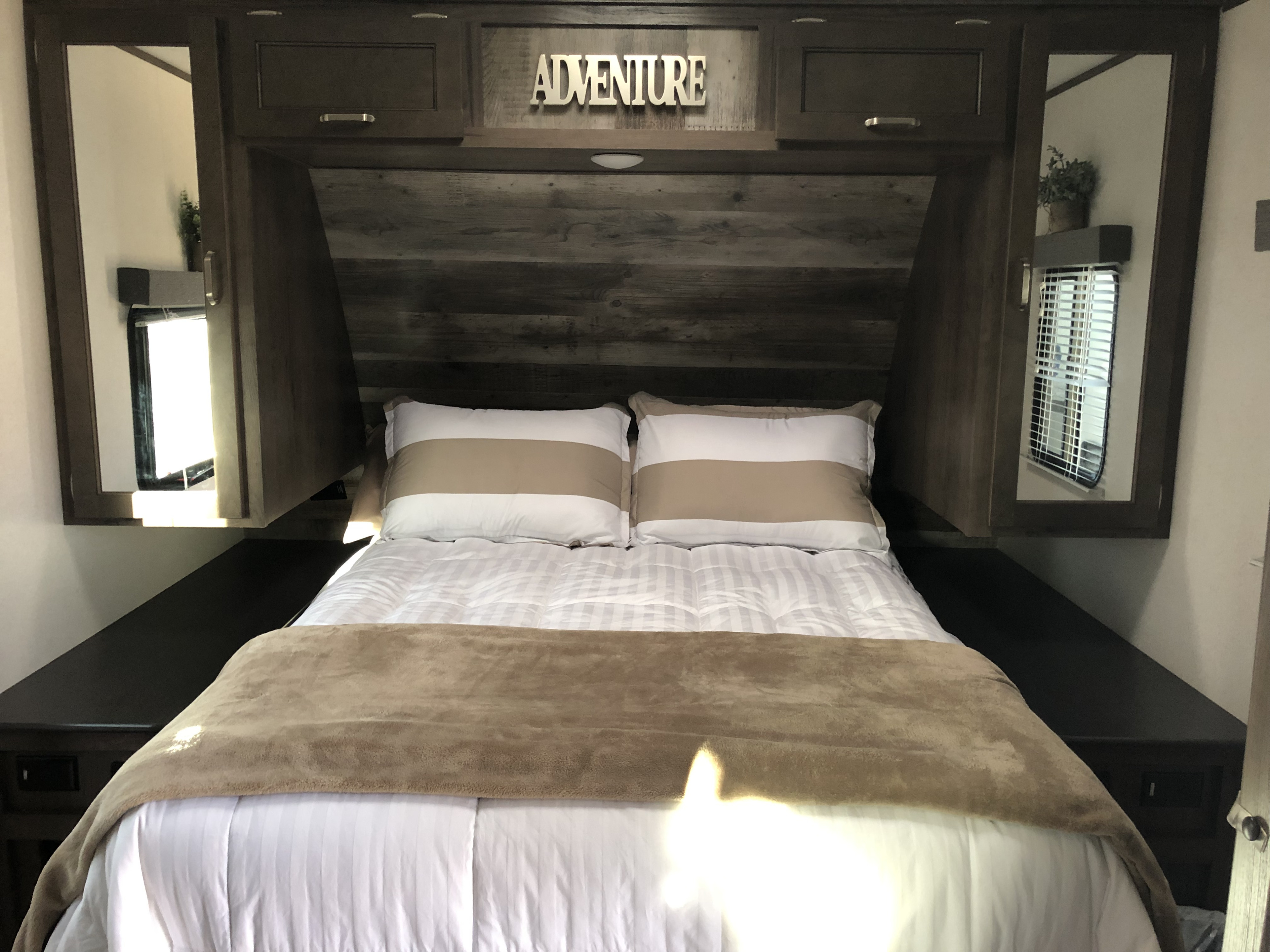 Cozy RV rental bedroom featuring a comfy bed with striped pillows, "ADVENTURE" sign, and mirrored storage.. Keystone RV Passport GT 2021