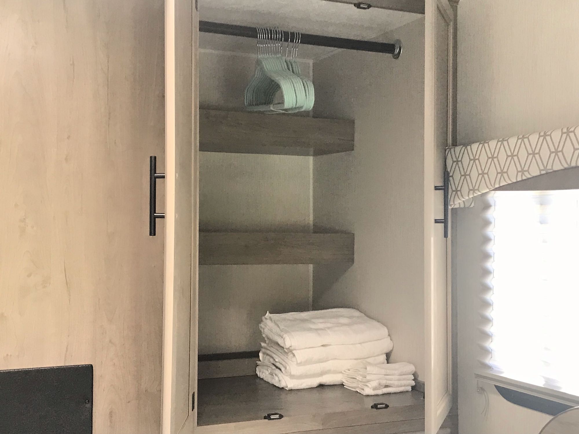 RV rental closet: Organized storage with a hanging rod, shelves, and neatly folded white towels.. Forest River Coachmen Freelander 2019