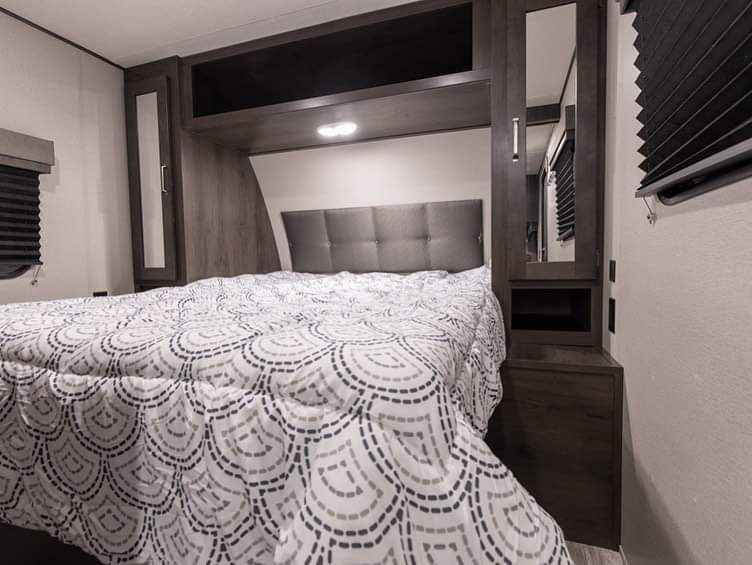 This RV rental bedroom offers a comfortable bed with a unique comforter, overhead storage, and mirrored wardrobes.. Grand Design 261bh 2022