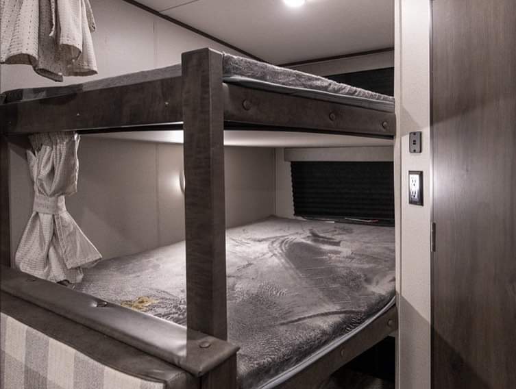 Inside this RV rental: stacked bunk beds with soft grey bedding, reading lights, and wall outlets for comfort.. Grand Design 261bh 2022