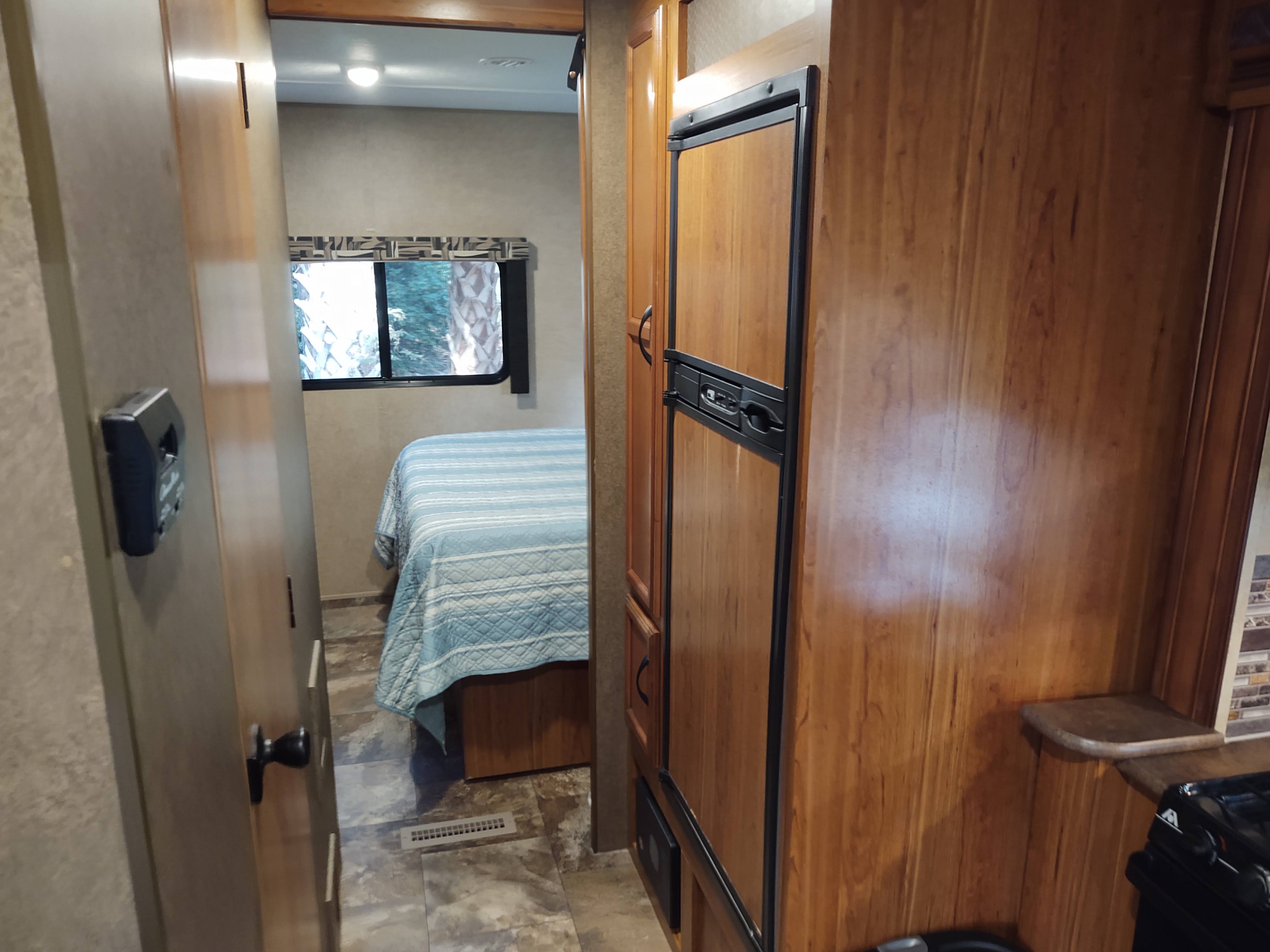 Inside an RV rental: A hallway view leads to a bedroom with blue striped bedding and a window. A built-in fridge is on the right.. Starcraft AR-One Maxx 2016