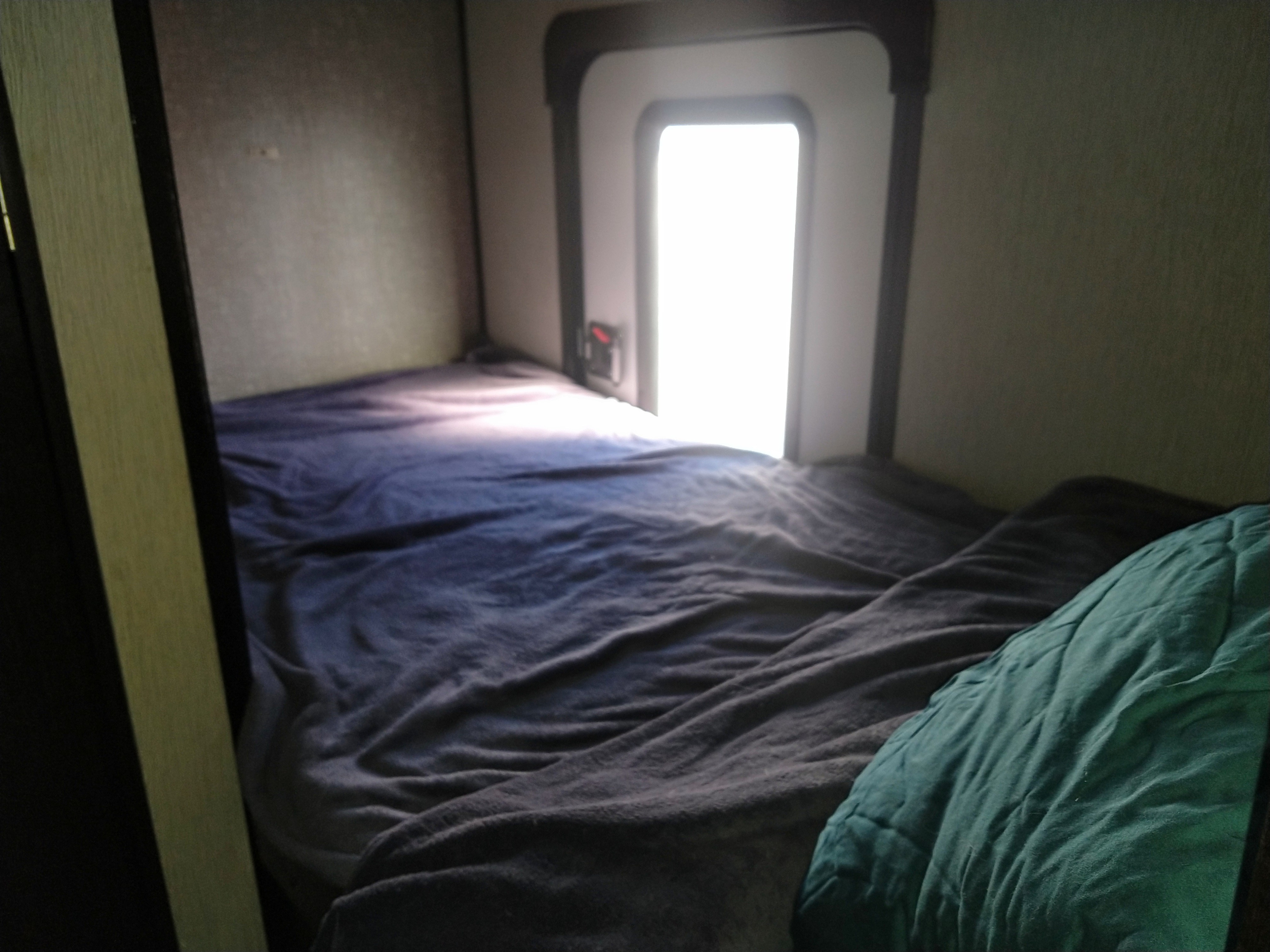 A comfortable RV rental bunk bed with dark blue bedding and a bright window offering natural light.. Heartland Mallard M185 2019