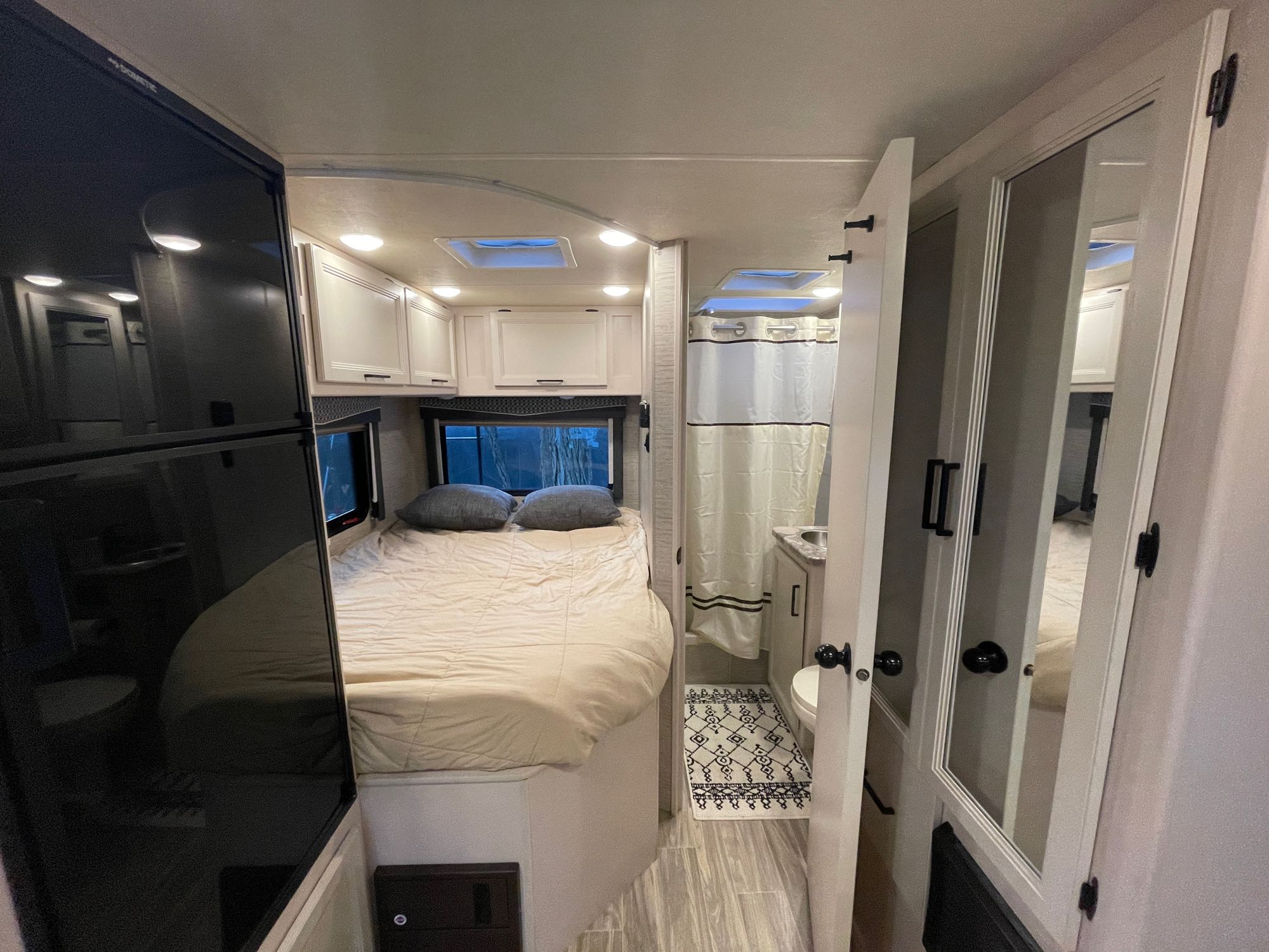 Modern RV rental interior with a cozy bedroom, compact bathroom, and large refrigerator. Ideal for comfortable travel.. Thor Four Winds 2021