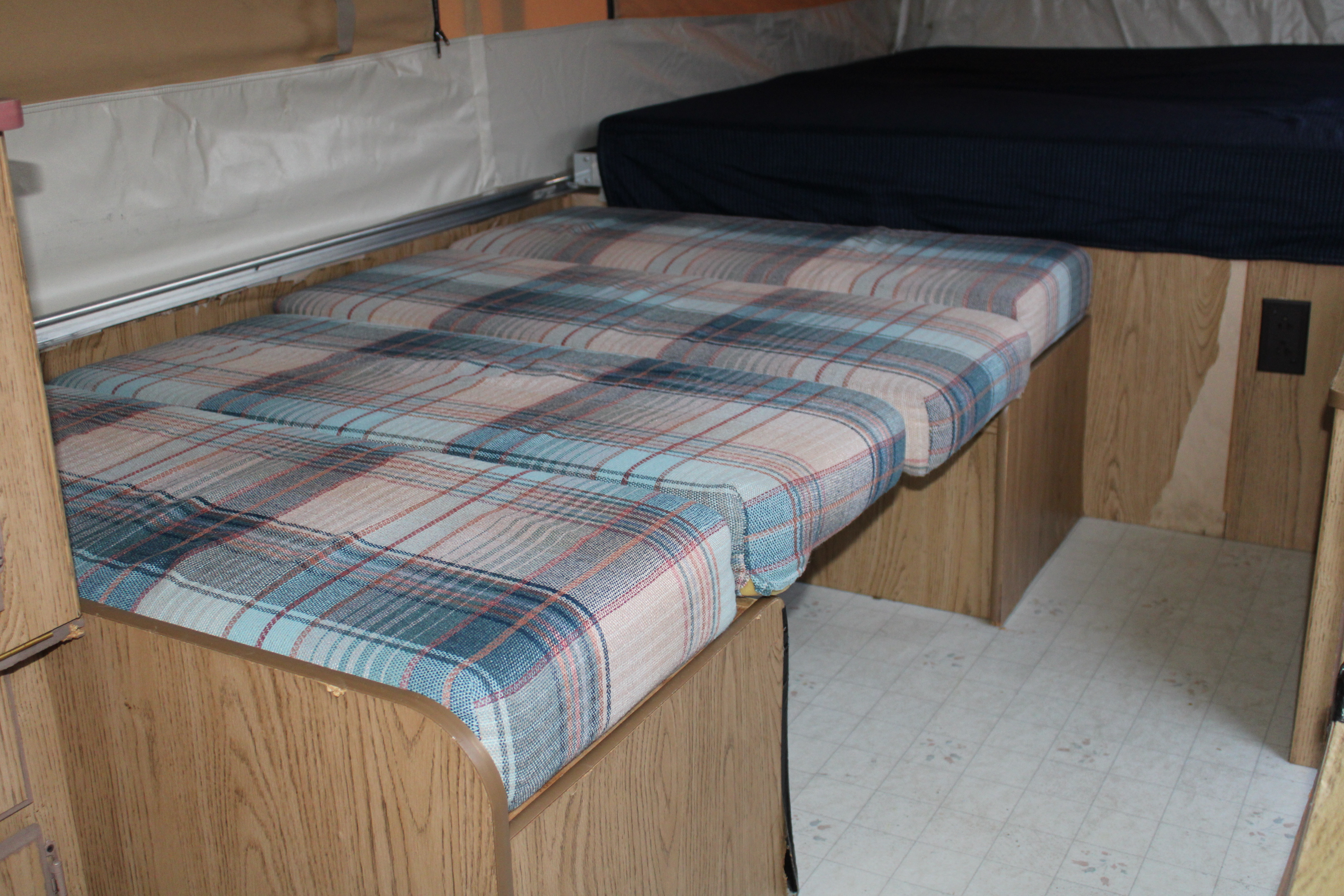 RV rental interior with plaid seating/bed area, a separate bed, and wood-paneled walls.. Coleman Destiny Royale 1992