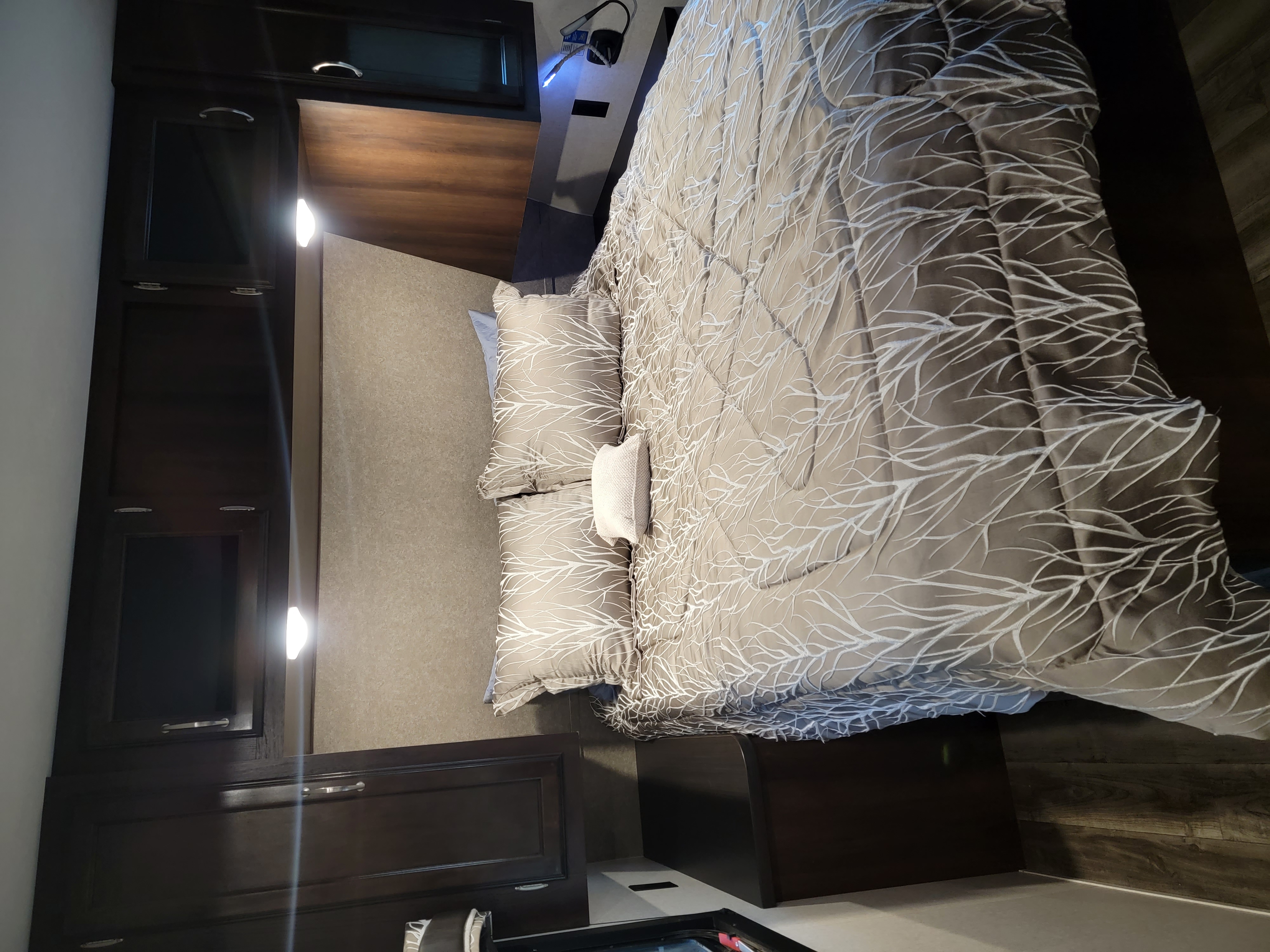 RV rental bedroom: a well-lit, cozy space with a large bed, patterned bedding, and dark wood overhead cabinets.. Jayco Jay Flight 2018