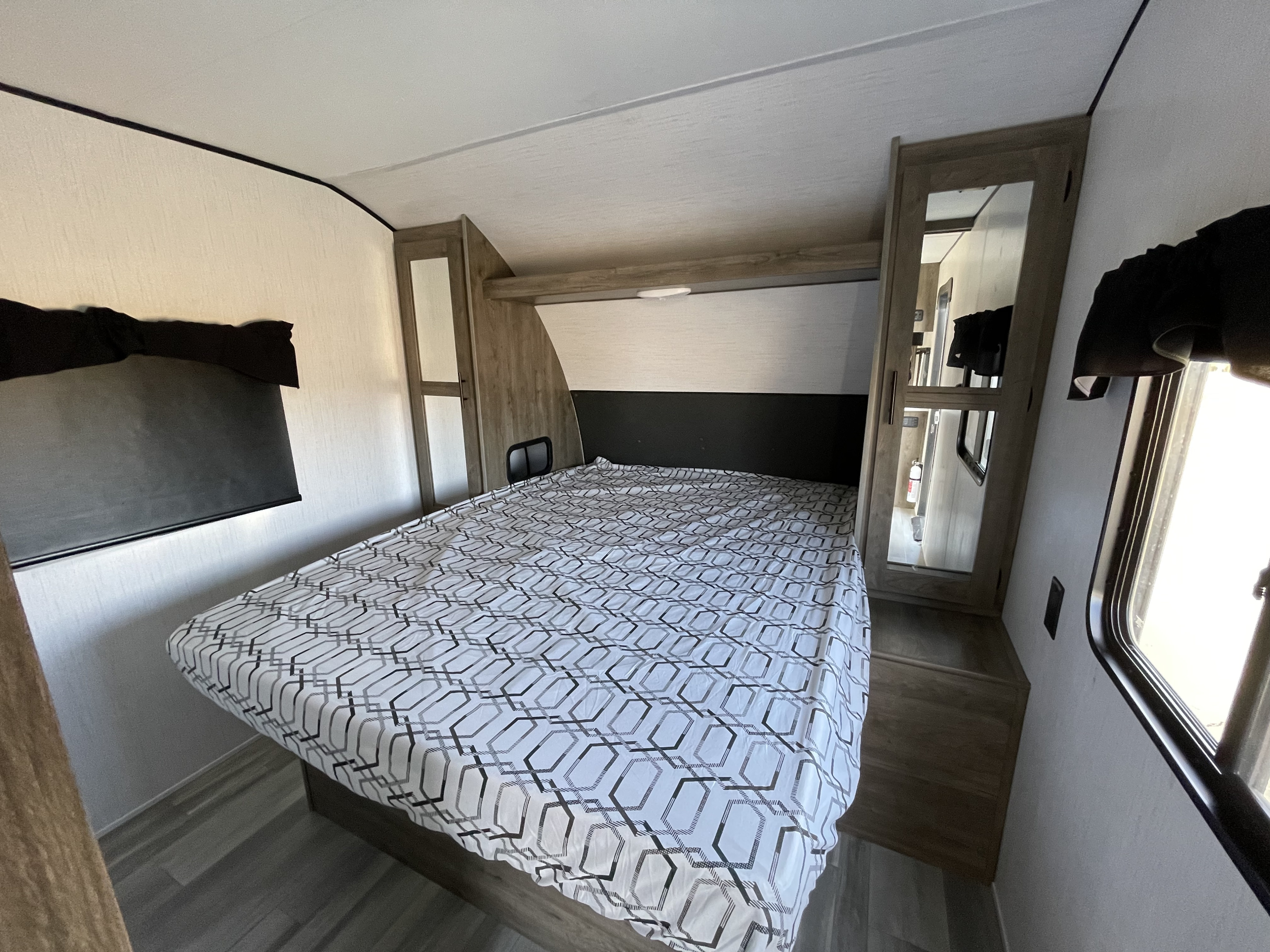 Inside this RV rental: a modern bedroom with a patterned bedspread, wood cabinetry, a mirrored closet, and a side window.. Pioneer BH270 2022