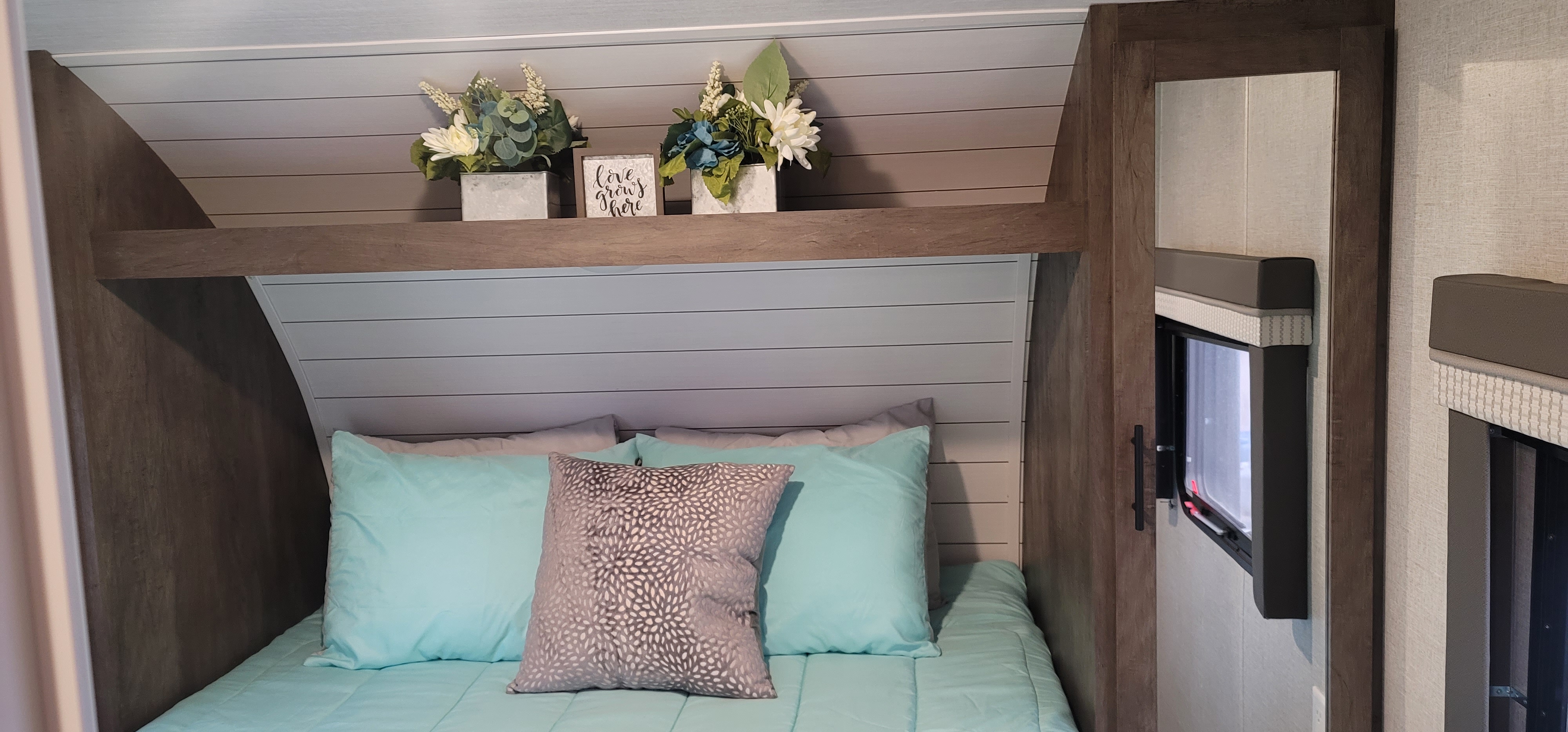 Comfortable RV rental interior featuring a bed with blue linens, a decorative shelf with flowers and a "love grows here" sign.. Forest River Salem Cruise Lite 2021