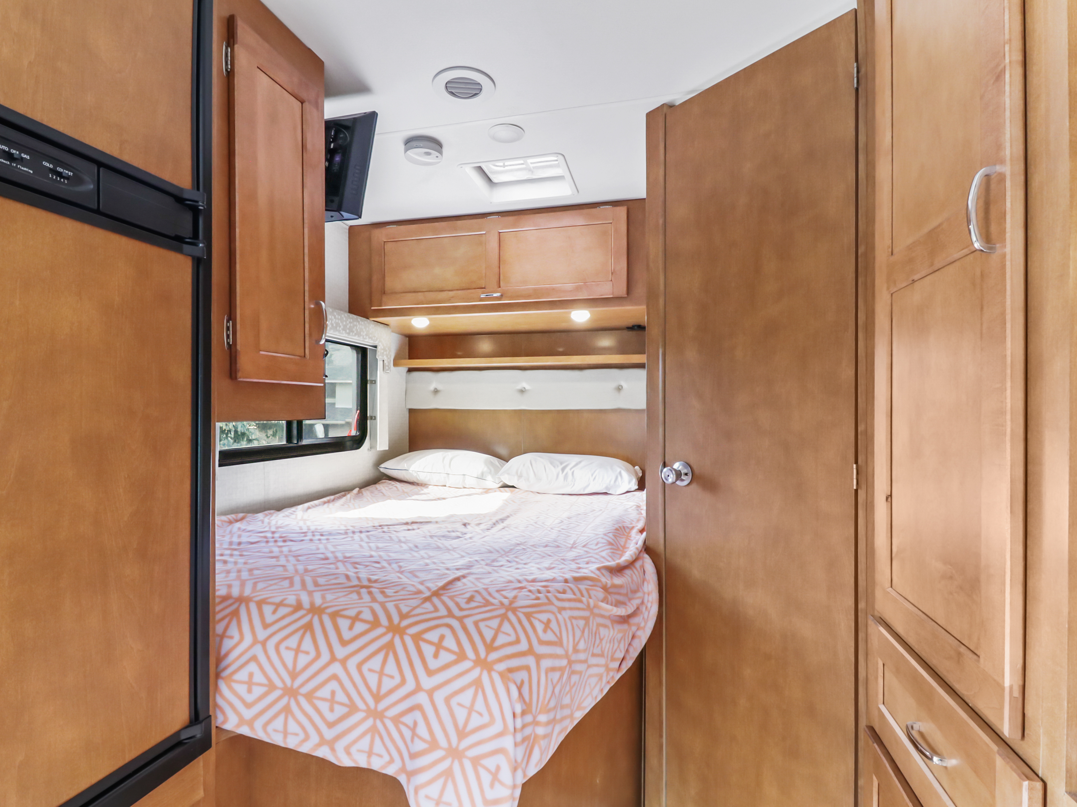 Explore the snug bedroom of this RV rental, featuring a cozy bed, window, and wood cabinetry for a comfortable camper stay.. Winnebago Other 2016