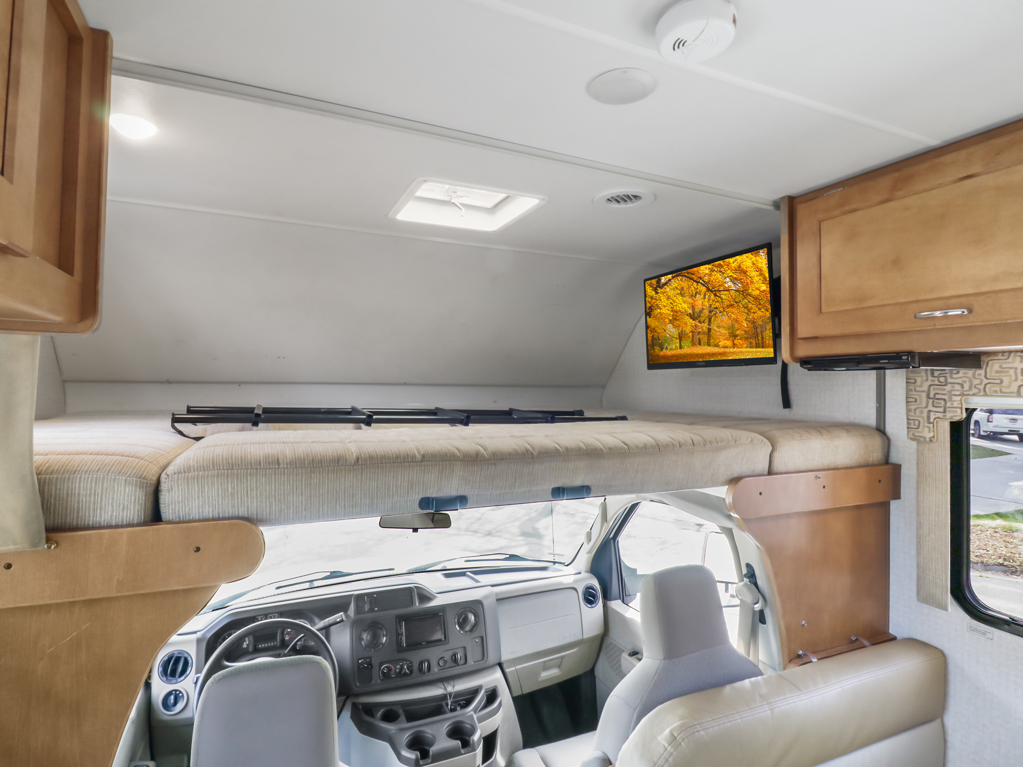 An RV rental interior with a comfy cab-over bunk bed, a TV showing fall foliage, and the driver's cockpit below.. Winnebago Other 2016