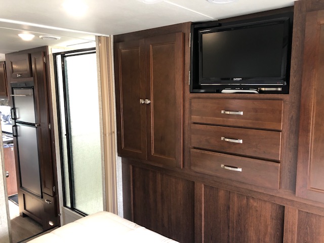 Cozy RV rental interior: bedroom with TV and storage, adjacent to a kitchenette and bathroom with frosted shower.. Forest River Forester 2017
