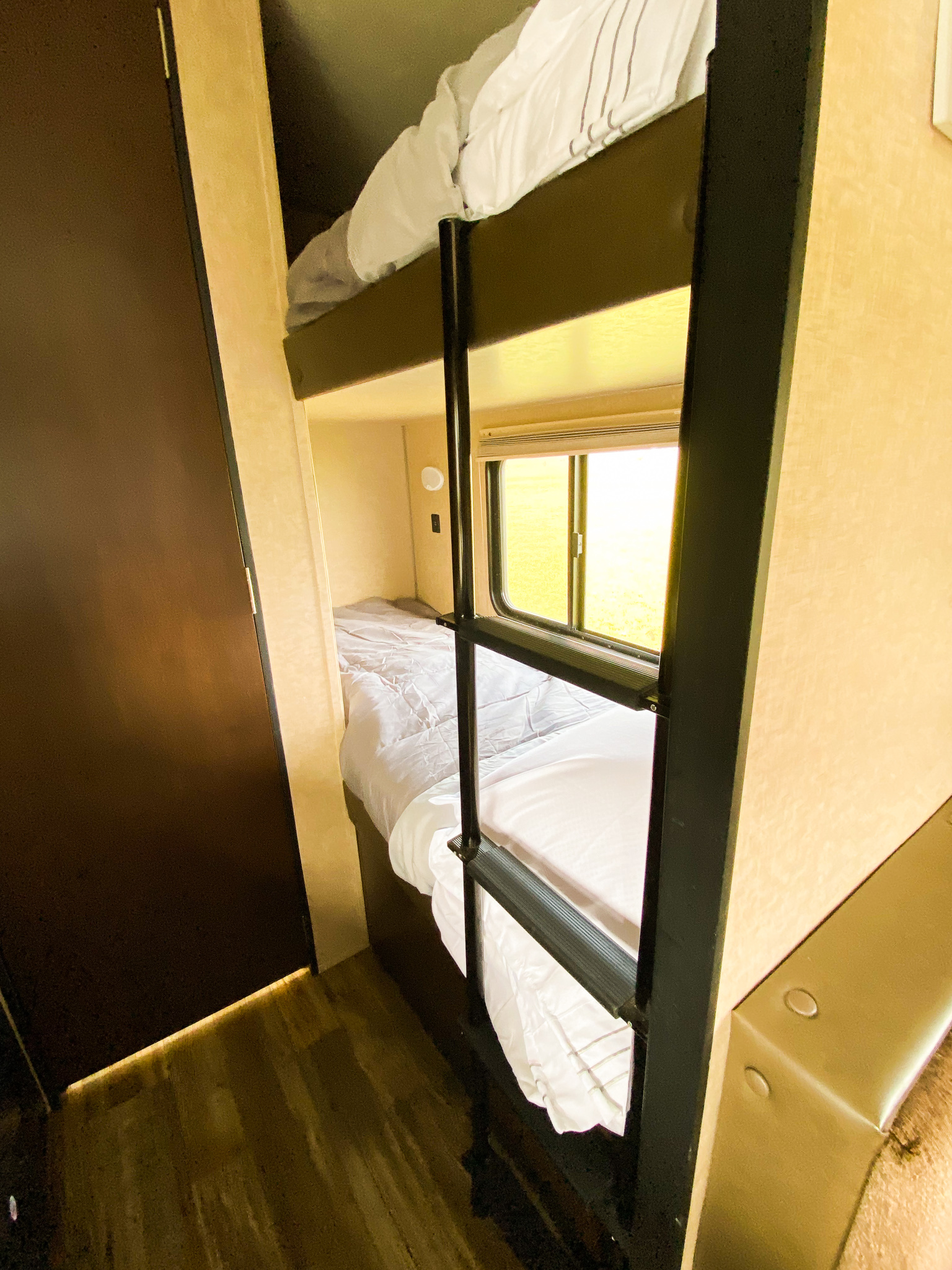 Cozy RV rental bunk beds with white bedding, a window, and a dark door on the left, designed for compact sleeping.. Forest River Cherokee Wolf Pup Cascade 2017