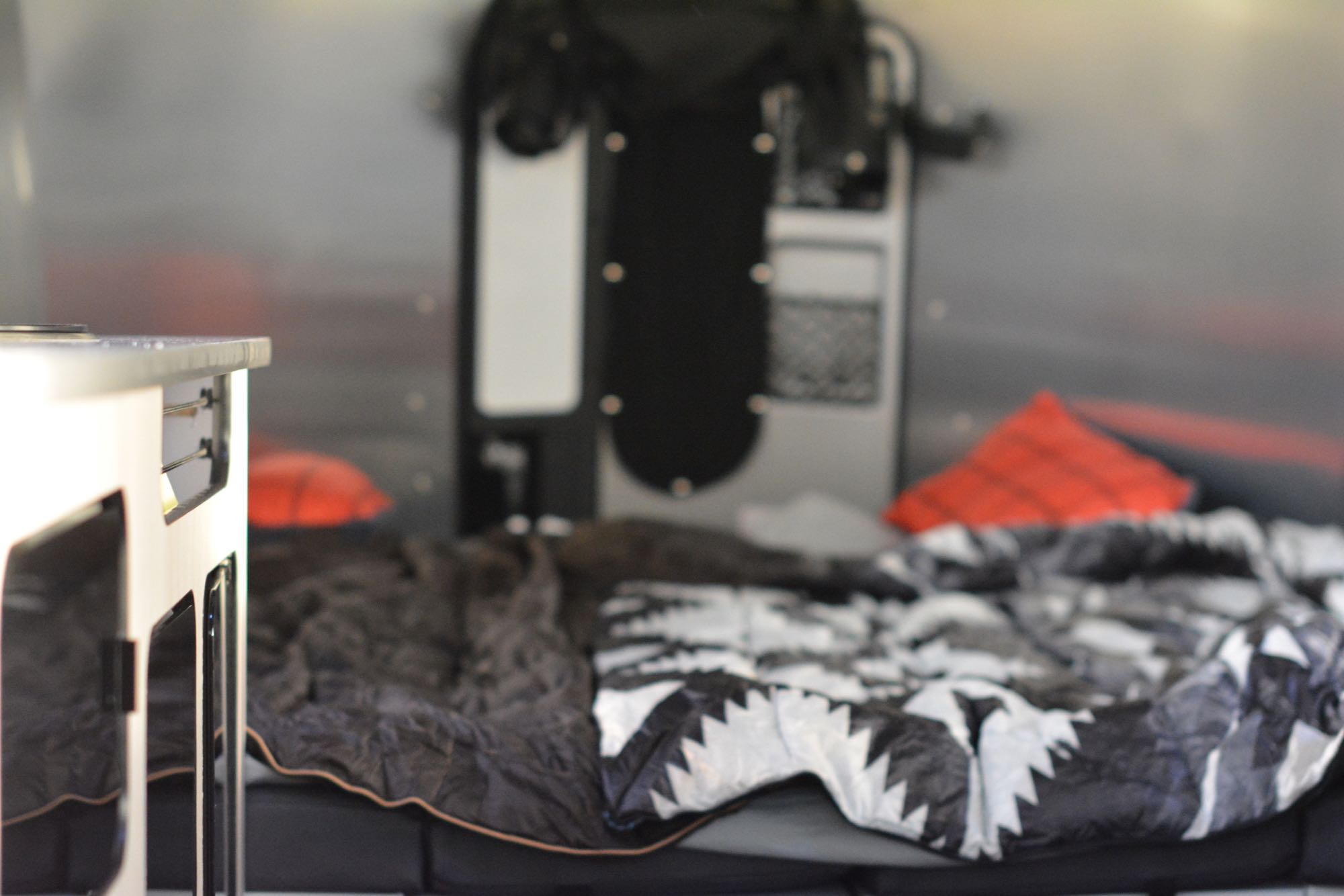 View inside an RV rental: a cozy sleeping area features a bed with patterned comforter and two orange pillows, beside a light counter.. Airstream Basecamp 20X 2022