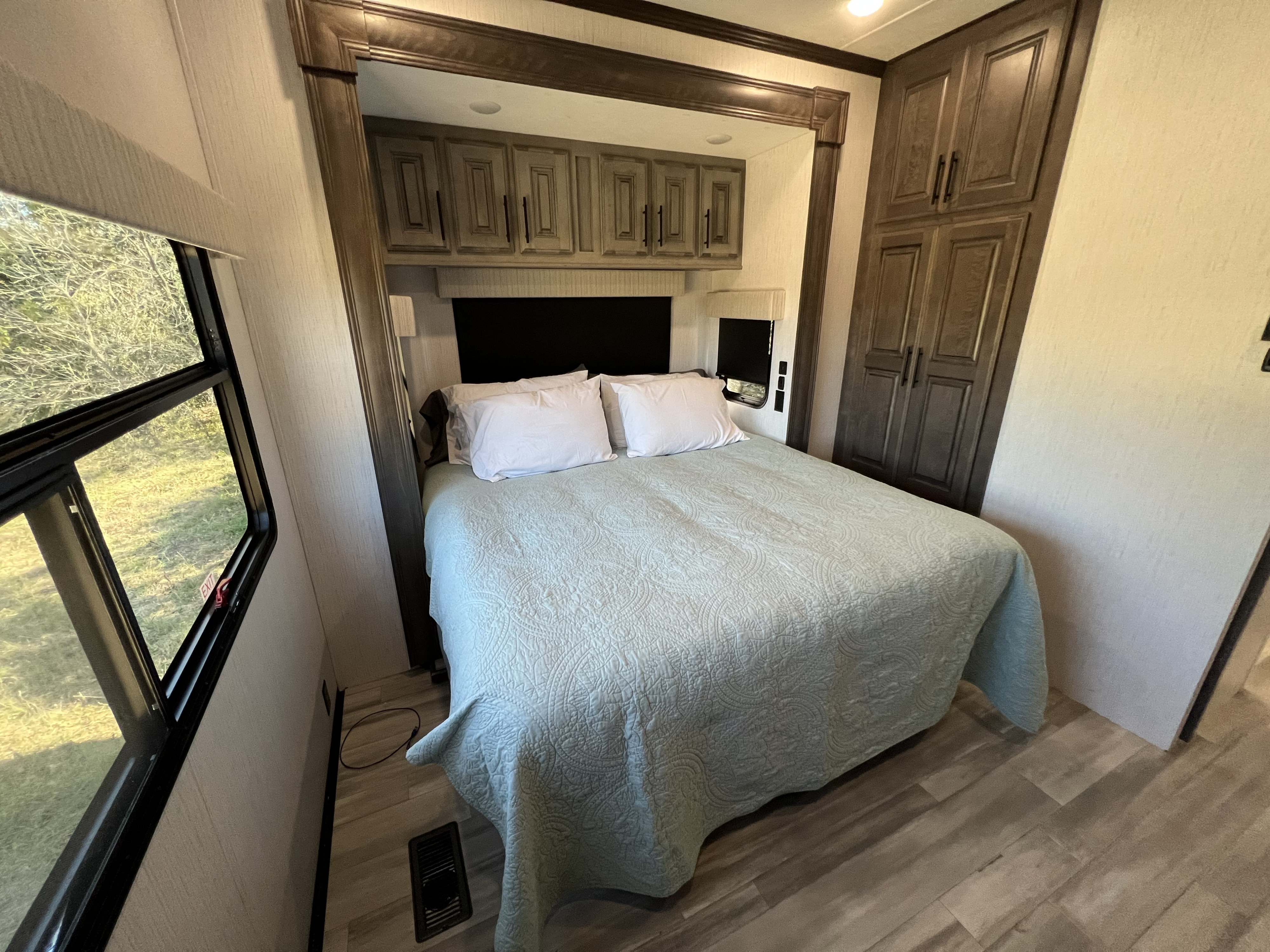 Inside a cozy RV rental bedroom. Features include a bed, overhead cabinets, wardrobe, and scenic windows.. Heartland Bighorn 2021