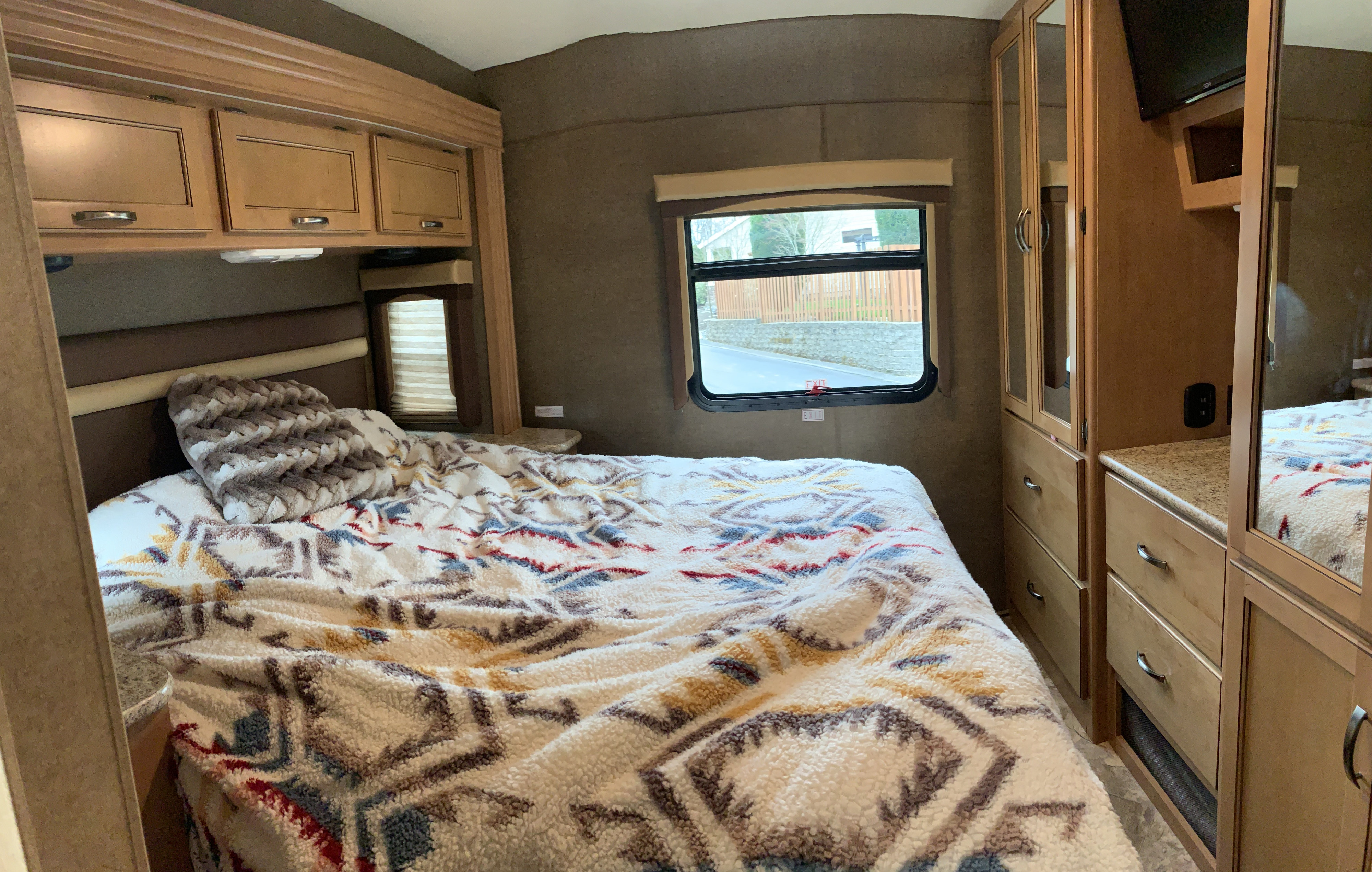 Cozy RV rental bedroom with patterned bedspread, overhead cabinets, window view, and mirrored closet storage.. Other A.C.E 2016