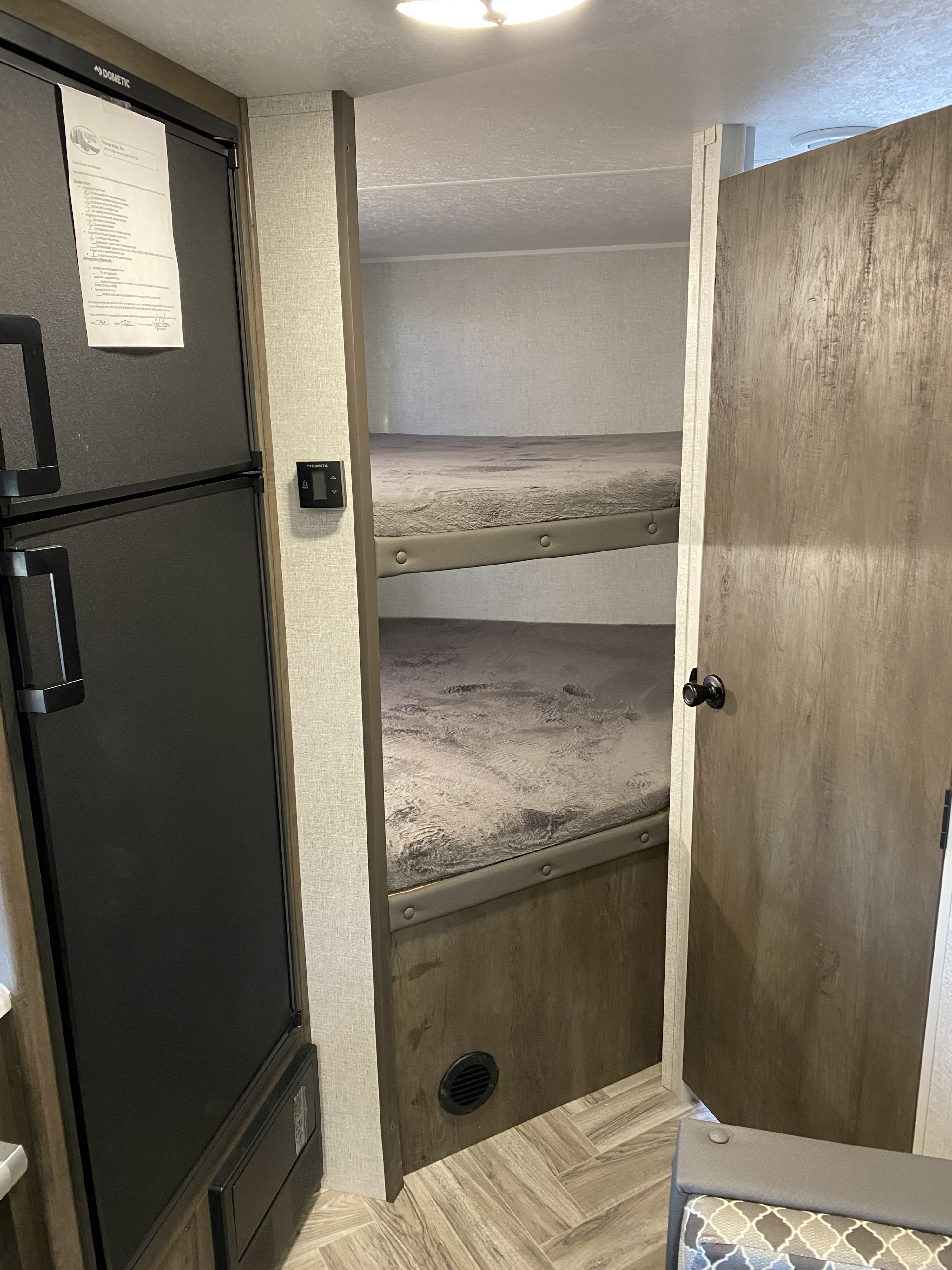 Inside an RV rental: a black Dometic refrigerator and a bunk bed area with two grey bunks, seen through an open door.. Forest River Evo 2021