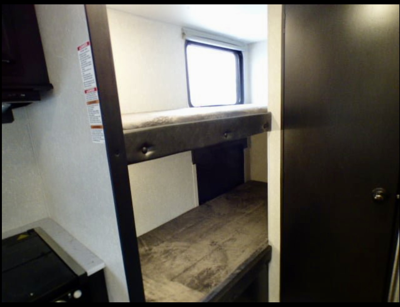 An RV rental's interior, showing sturdy bunk beds with a window, a partial kitchen counter, and a dark door.. Forest River Cherokee Wolf Pup 2021