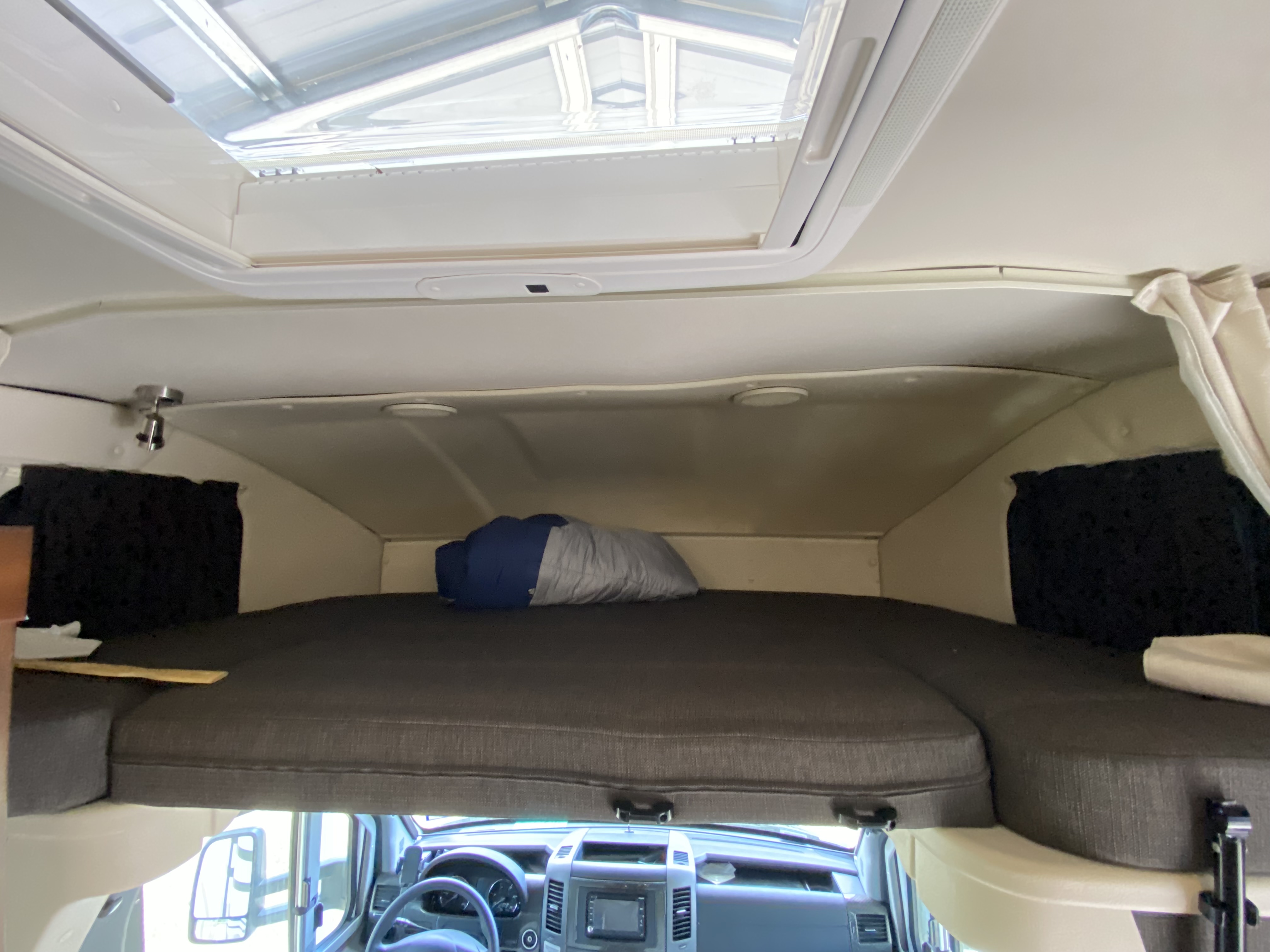 Spacious cab-over bunk bed in an RV rental, featuring a skylight above and the vehicle's dashboard below.. Winnebago View 2015