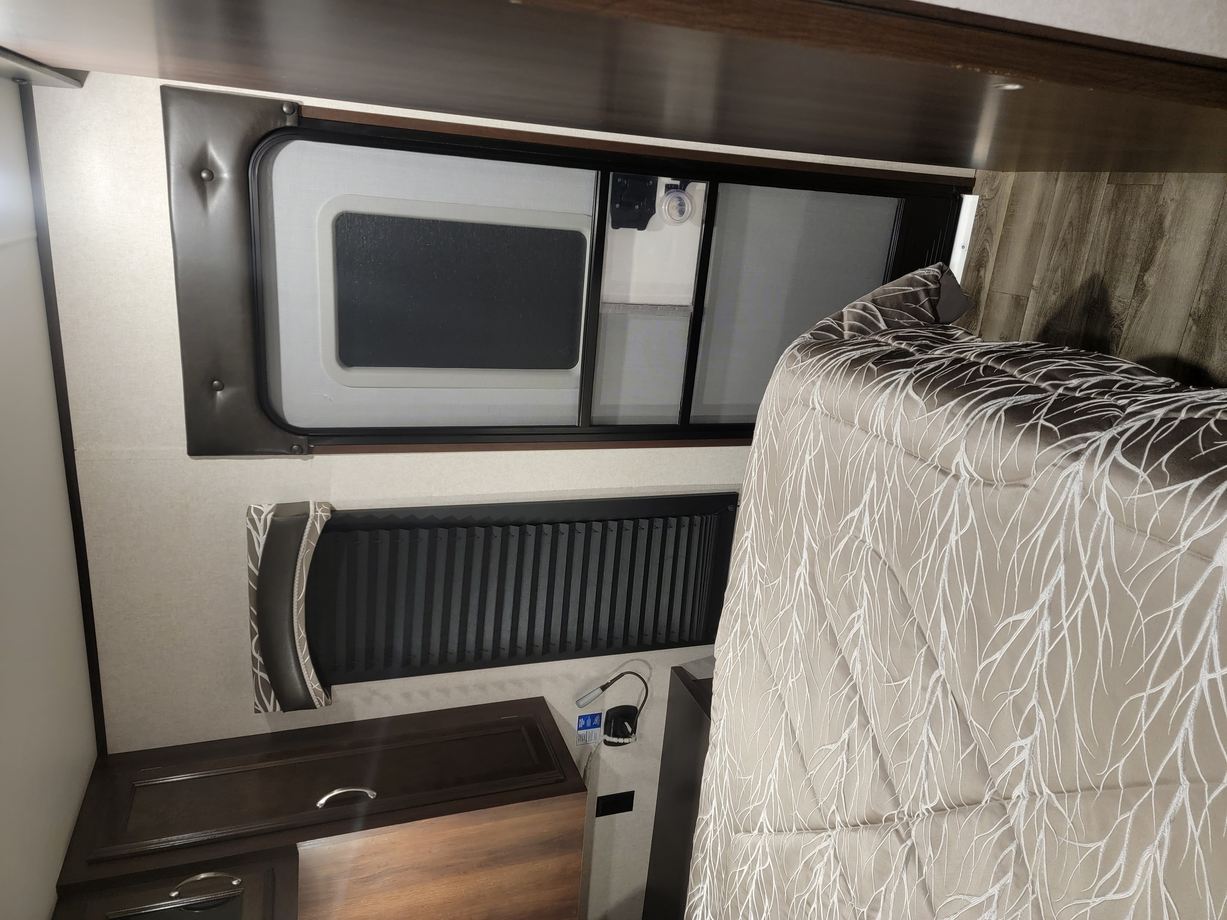 Cozy RV rental bedroom: bed with branch-patterned comforter, window with blind, and cabinet.. Jayco Jay Flight 2018