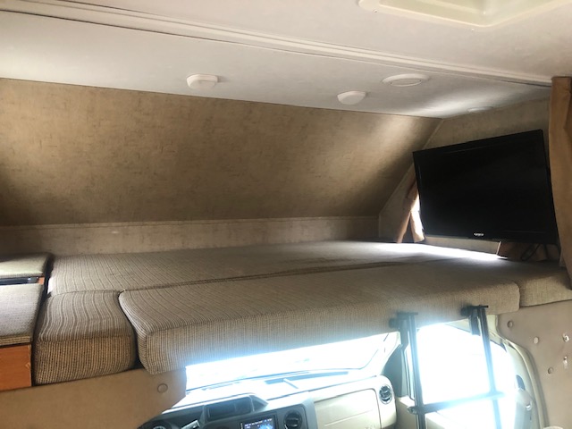 Explore an RV rental: a spacious cab-over bunk sleeping area with a mounted TV and a ladder for access.. Forest River Sunseeker 2016